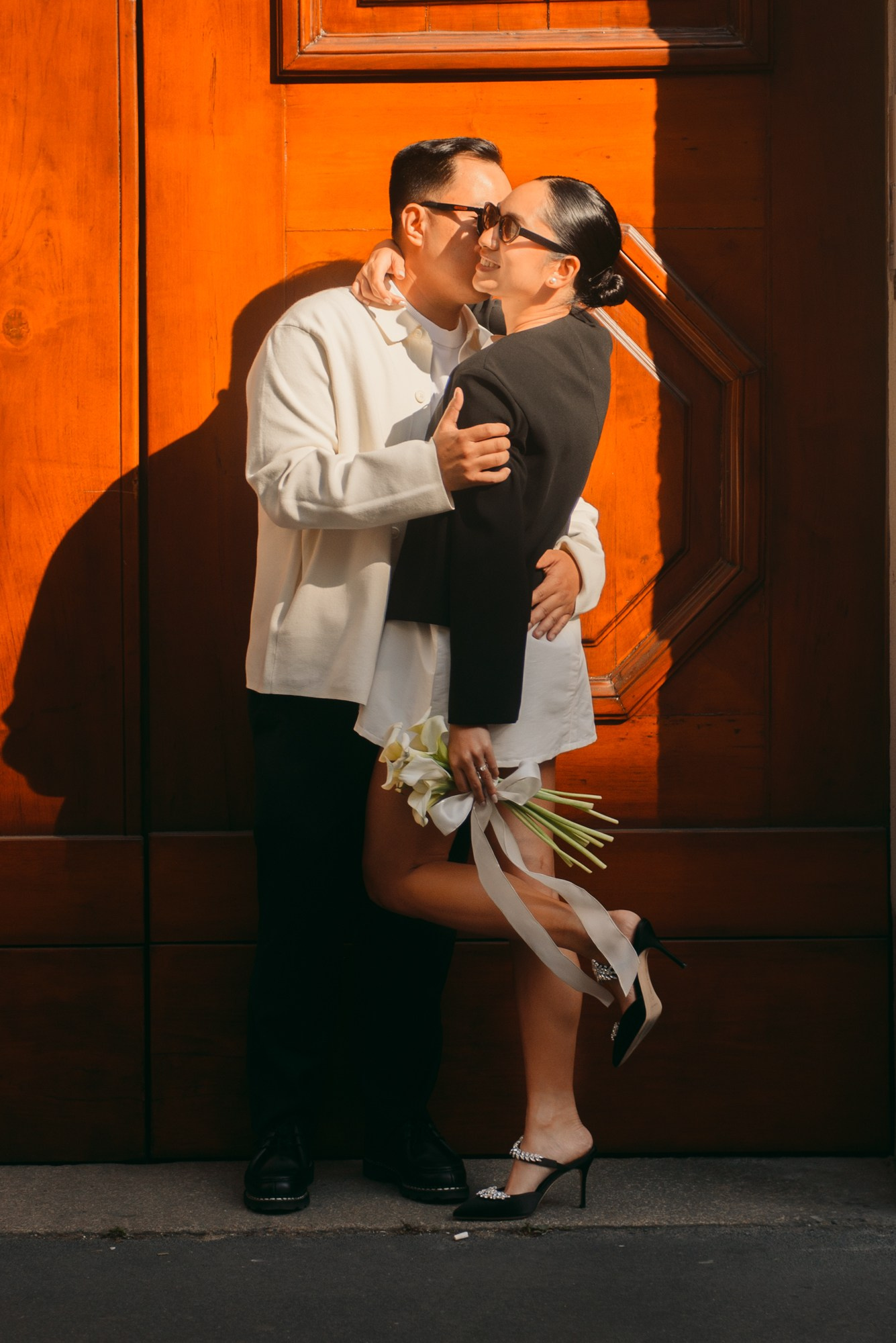 Romantic urban couple photoshoot captured in warm golden light. The couple embraces in front of a large wooden door, creating a modern, intimate and cinematic mood. Perfect for civil weddings, elopements and love story photography in Italy. urban couple photoshoot, elopement Italy, Milan wedding photographer, love story photography, modern wedding couple, romantic city photos, engagement shoot Italy, cinematic couple session