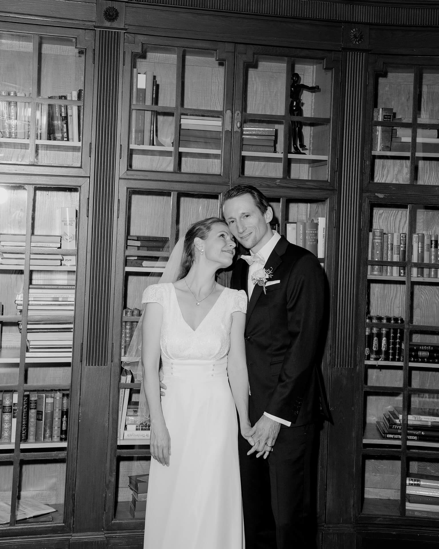 Black and white newlyweds standing in library, luxury wedding portrait