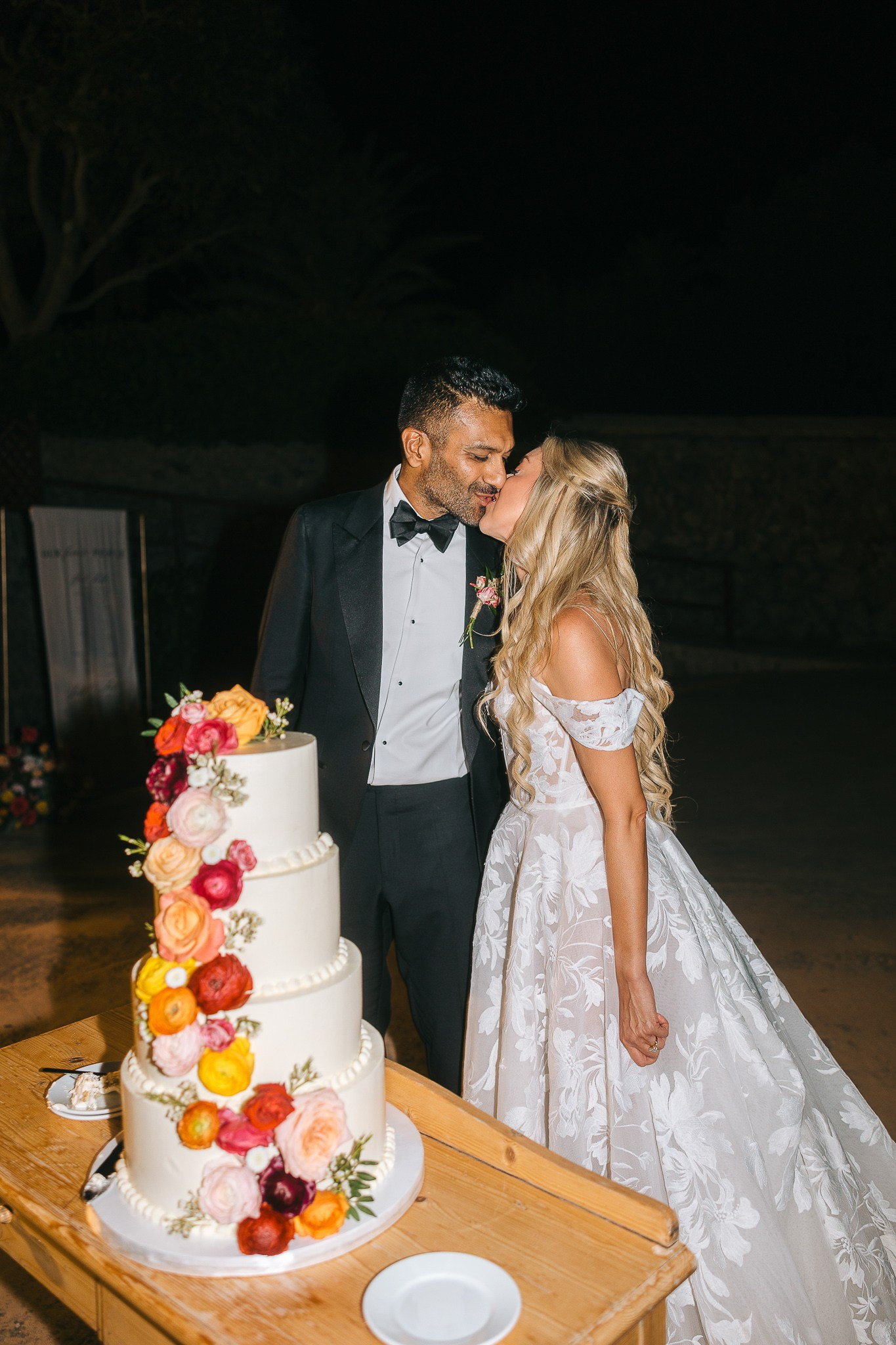 Bride and groom kissing beside their four-tier floral wedding cake at their Mallorca reception