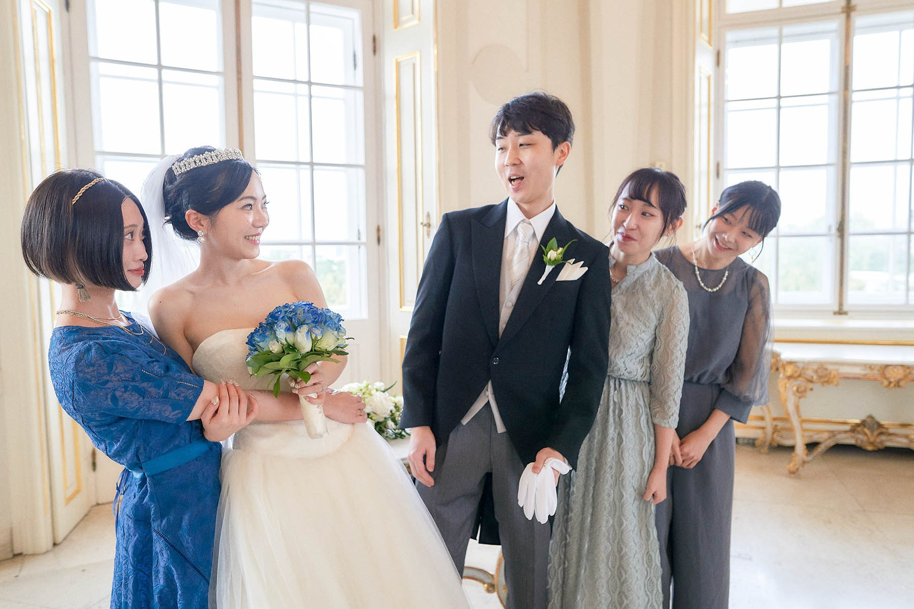 Bride's best friend pulling her away as groom smiles at reception.
