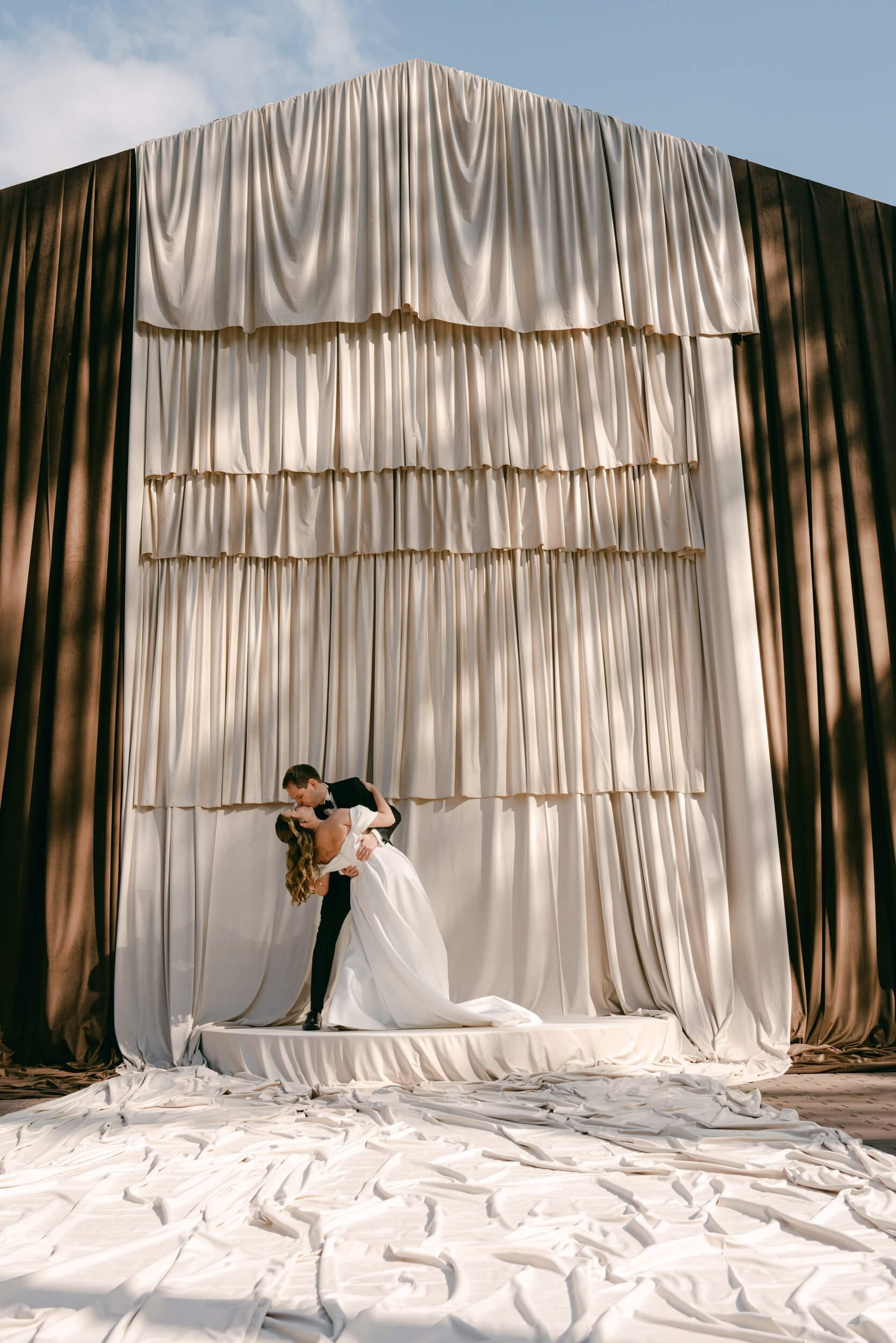 Wedding portraits, couple kisses on draped stage with flowing fabric