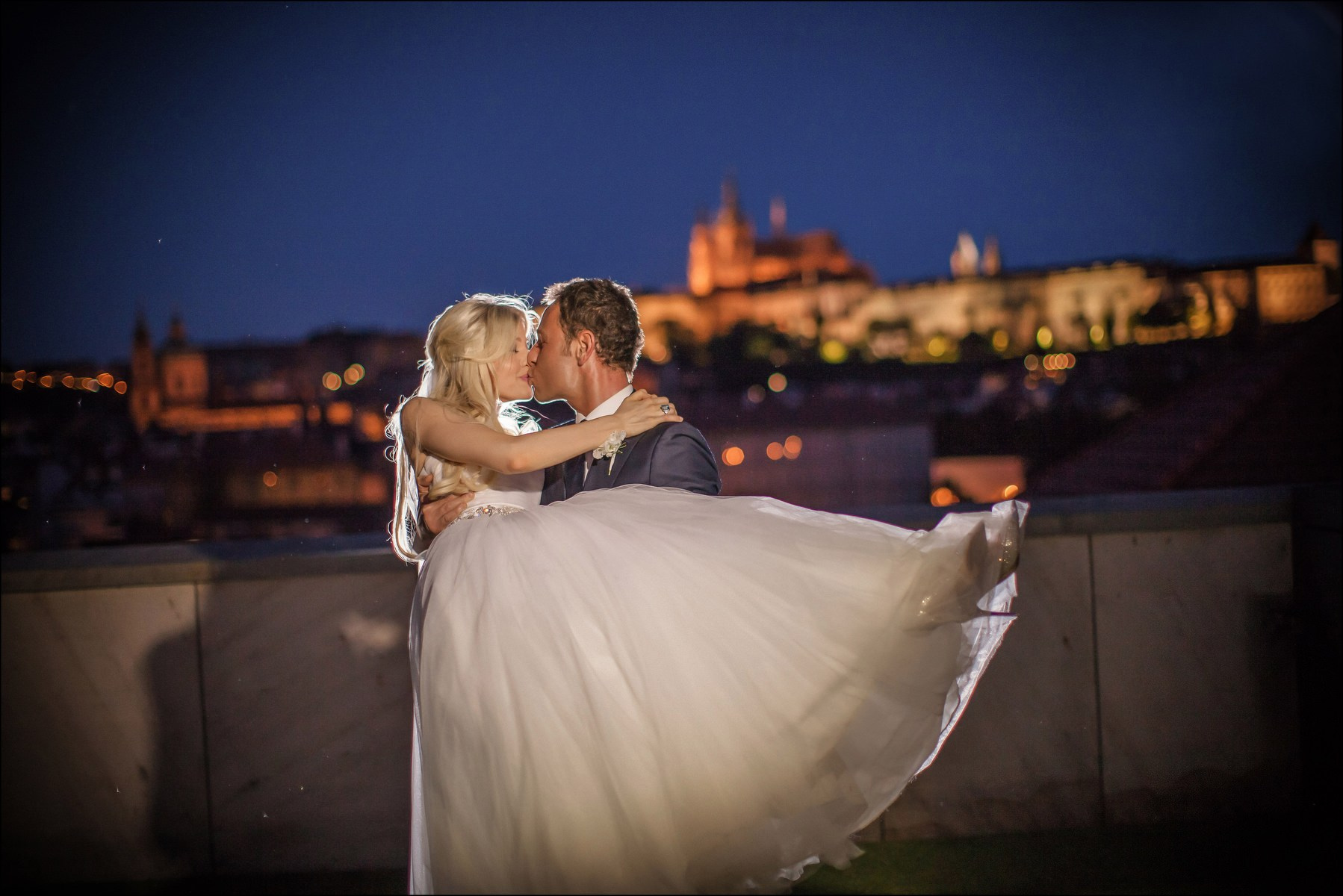 Groom lifting bride embrace nighttime Prague Castle view