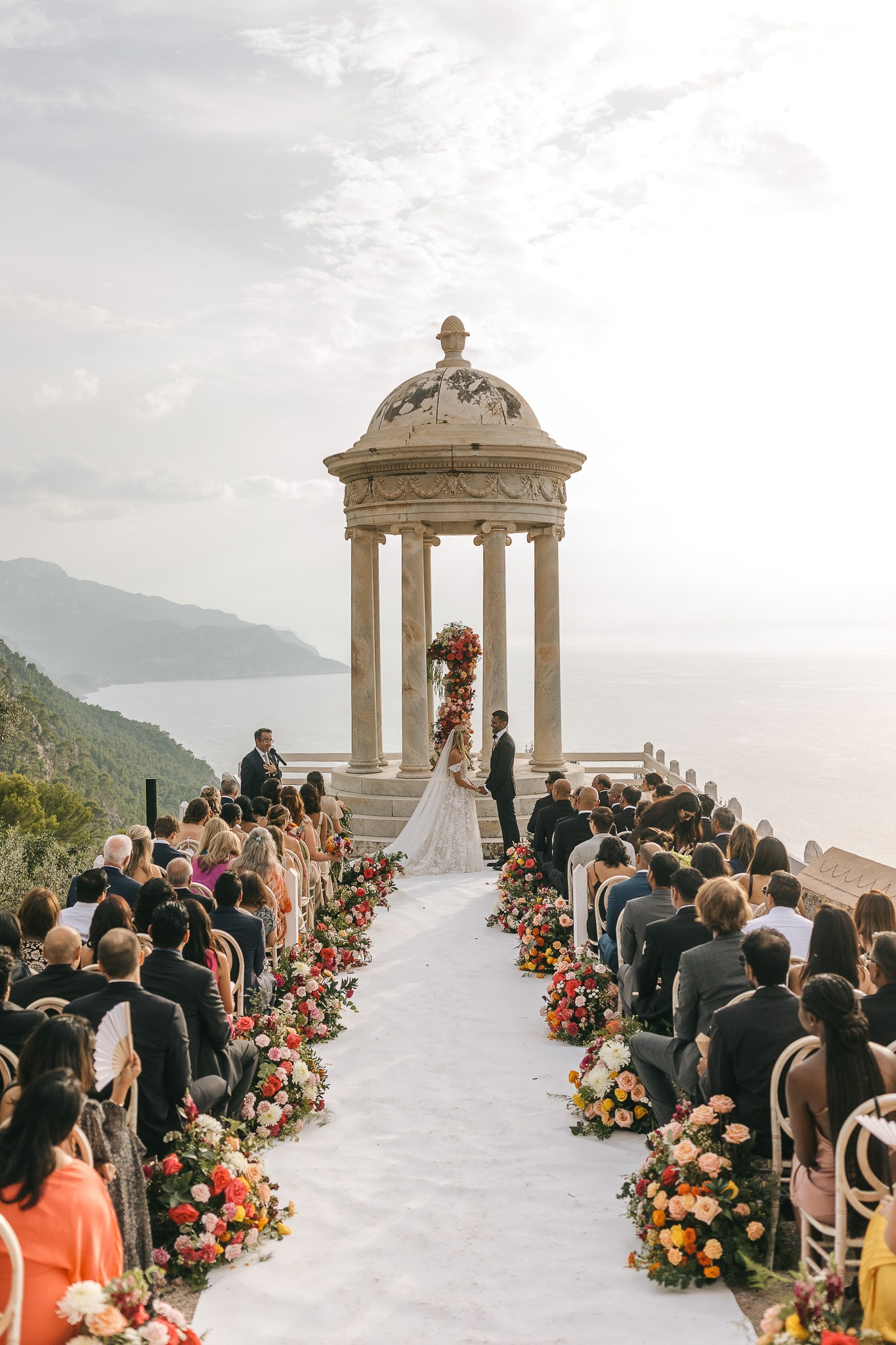 Wide view of the wedding ceremony at Son Marroig with bride, groom, and their wedding officiant overlooking the sea