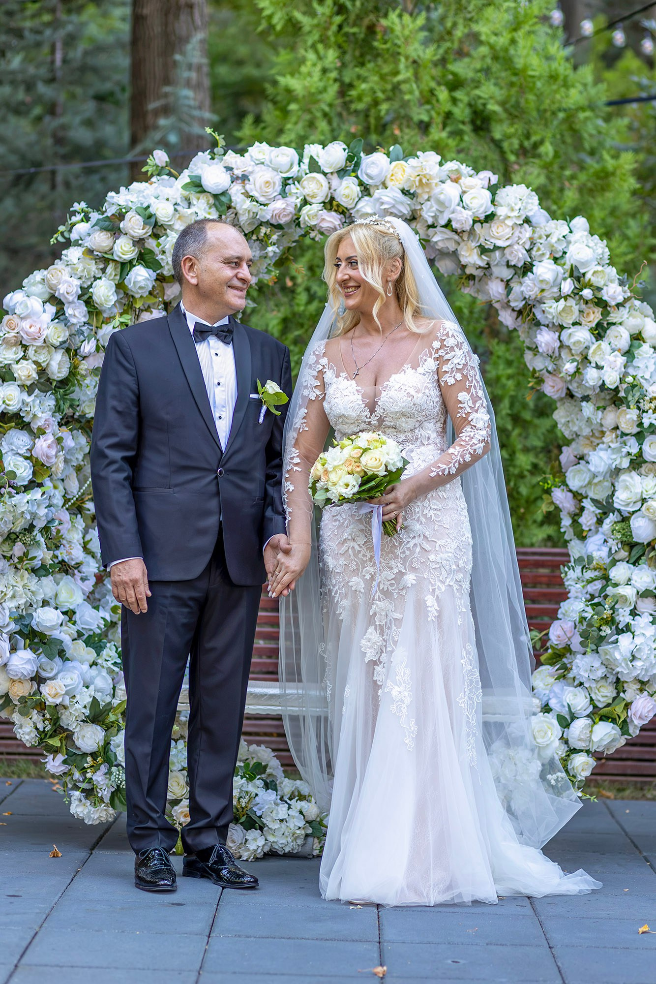 Ședință foto nuntă lângă arcada florală, mirii se țin de mană