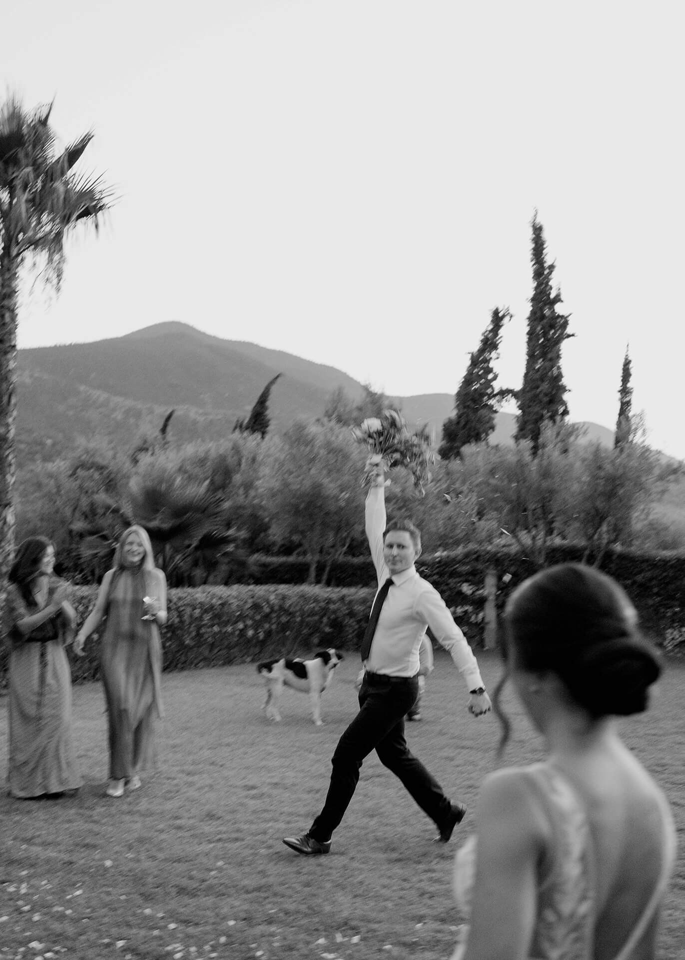 Wedding guest strides across lawn holding bouquet overhead