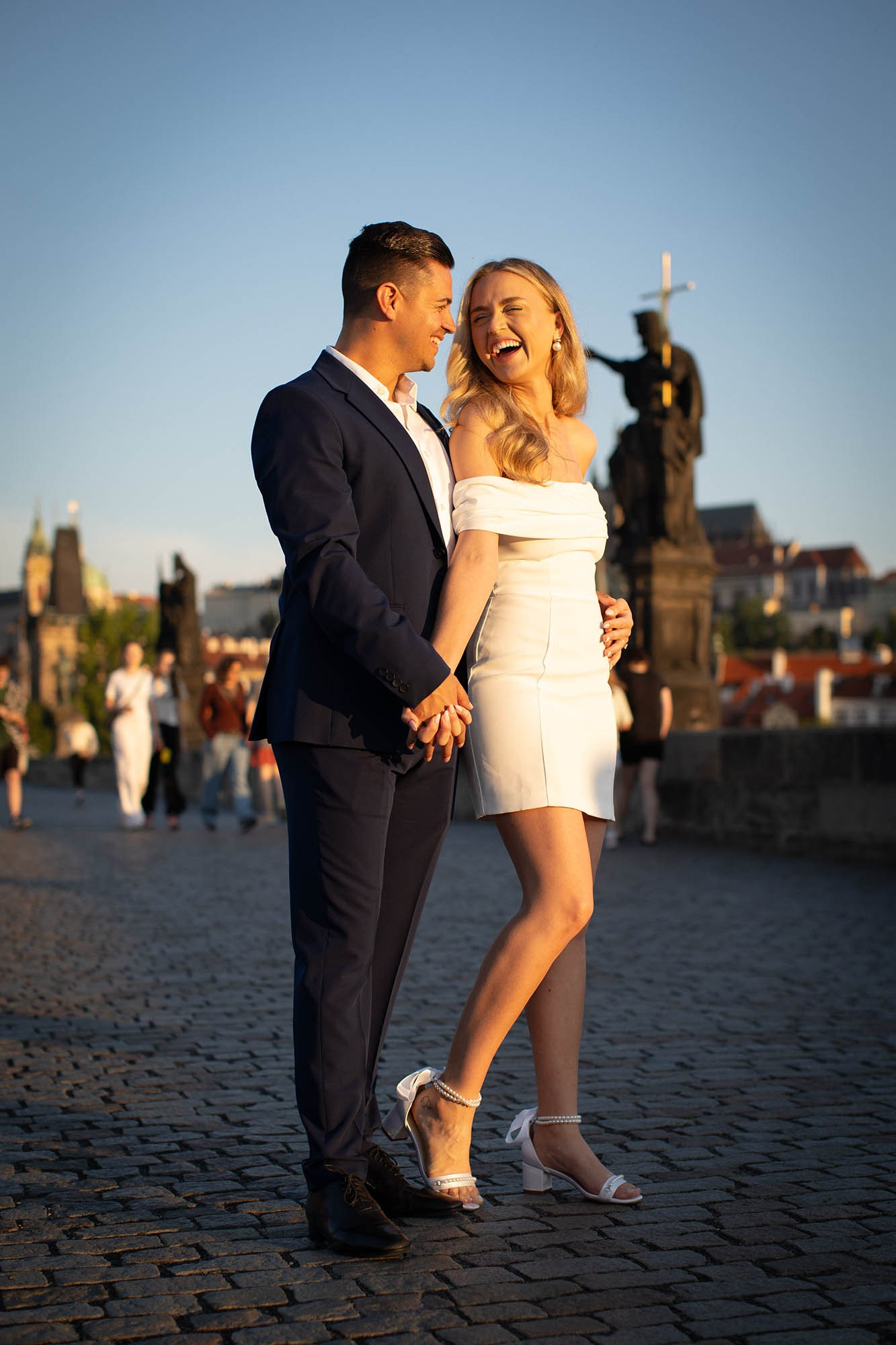 Playful engaged couple posing in golden hour atop Charles Bridge.