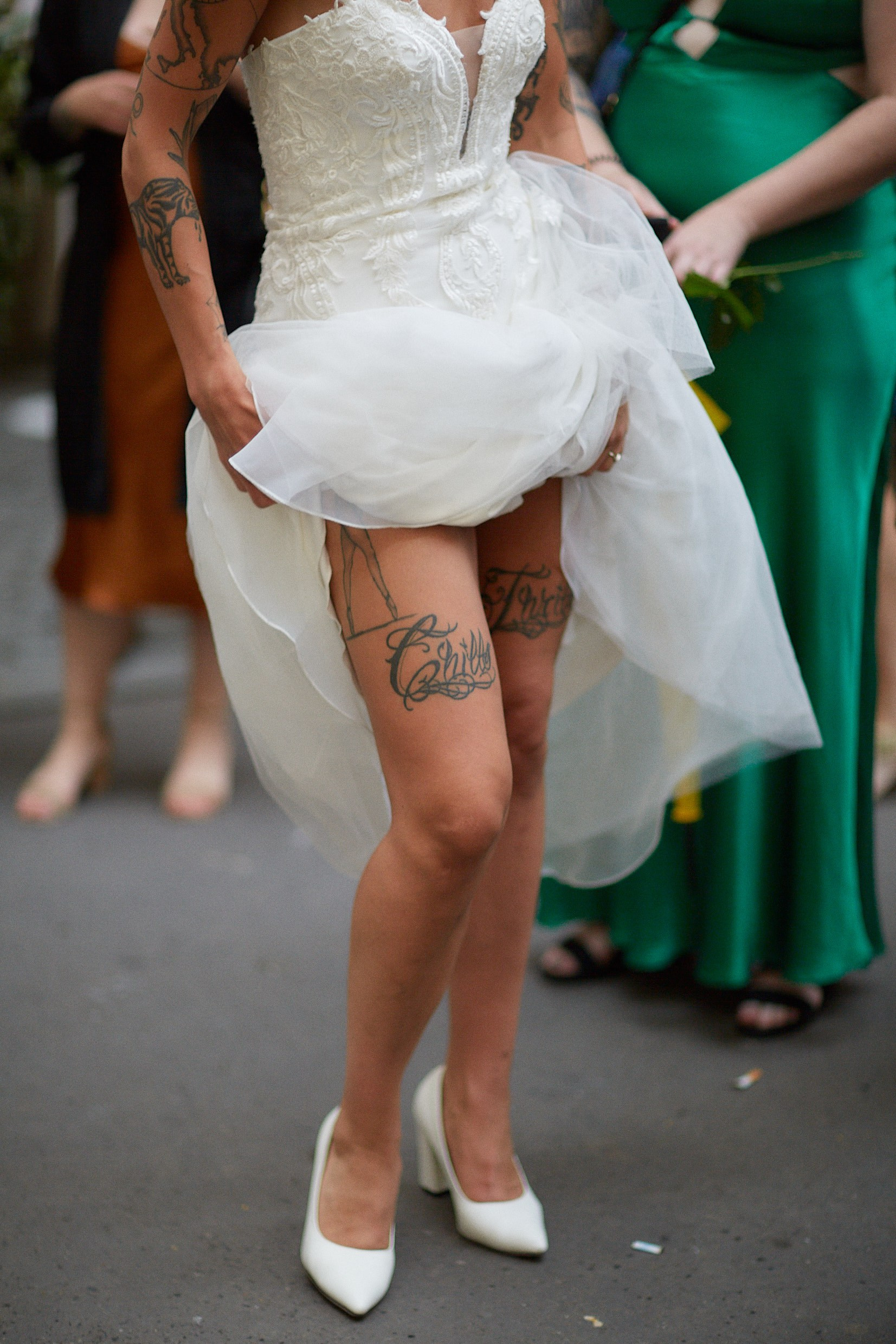 Tattooed burlesque bride revealing leg art before entering chapel.