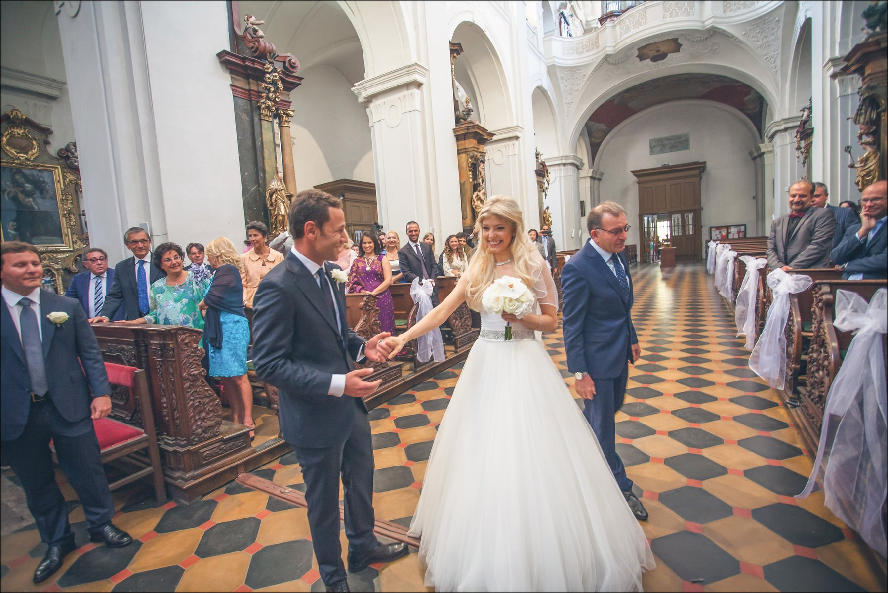 Groom taking bride's hand from father at altar St. Thomas Church Prague