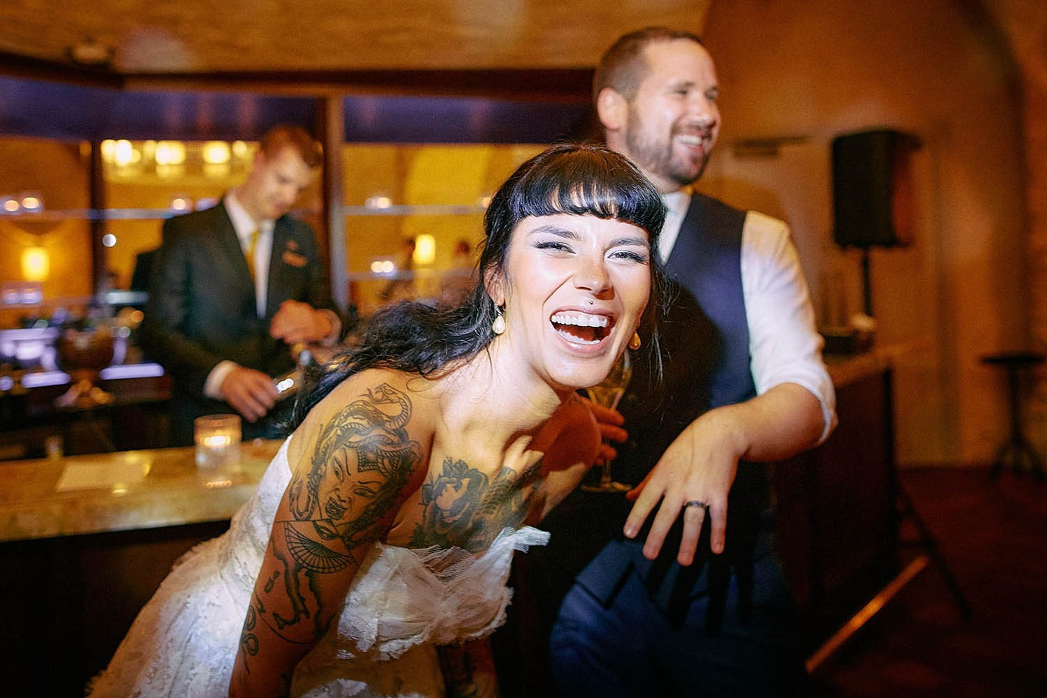 Tattooed bride bursting with laughter beside smiling groom