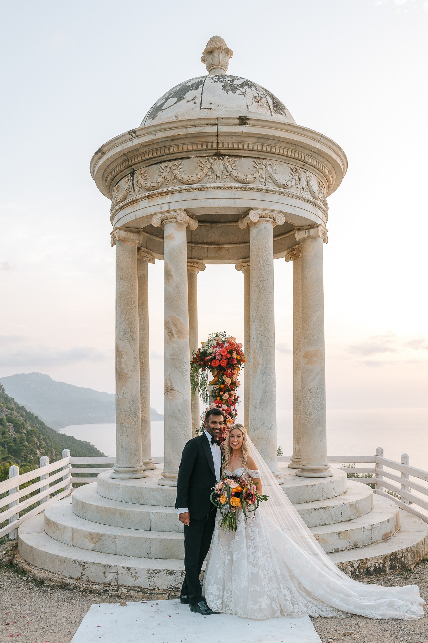 Bride and groom posing in the Son Marroig temple with their colorful bouquet at sunset