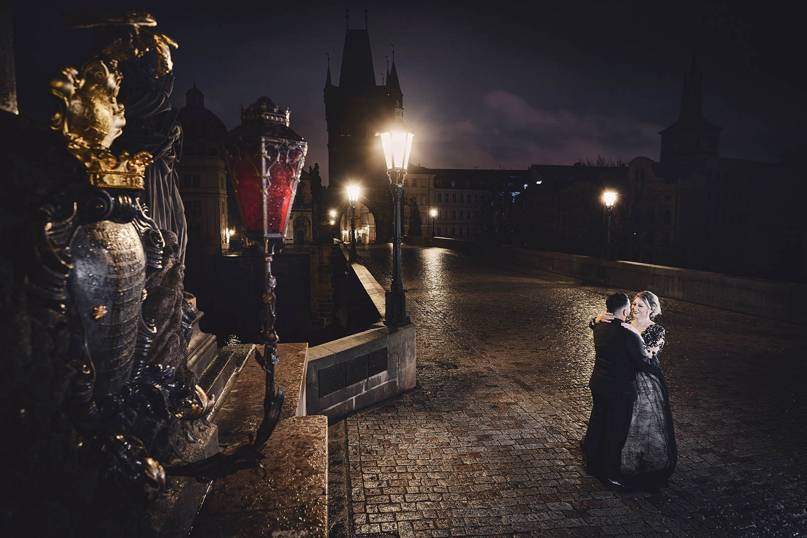 Couple dressed in all black walk through the empty landscape of Prague atop the Charles Bridge