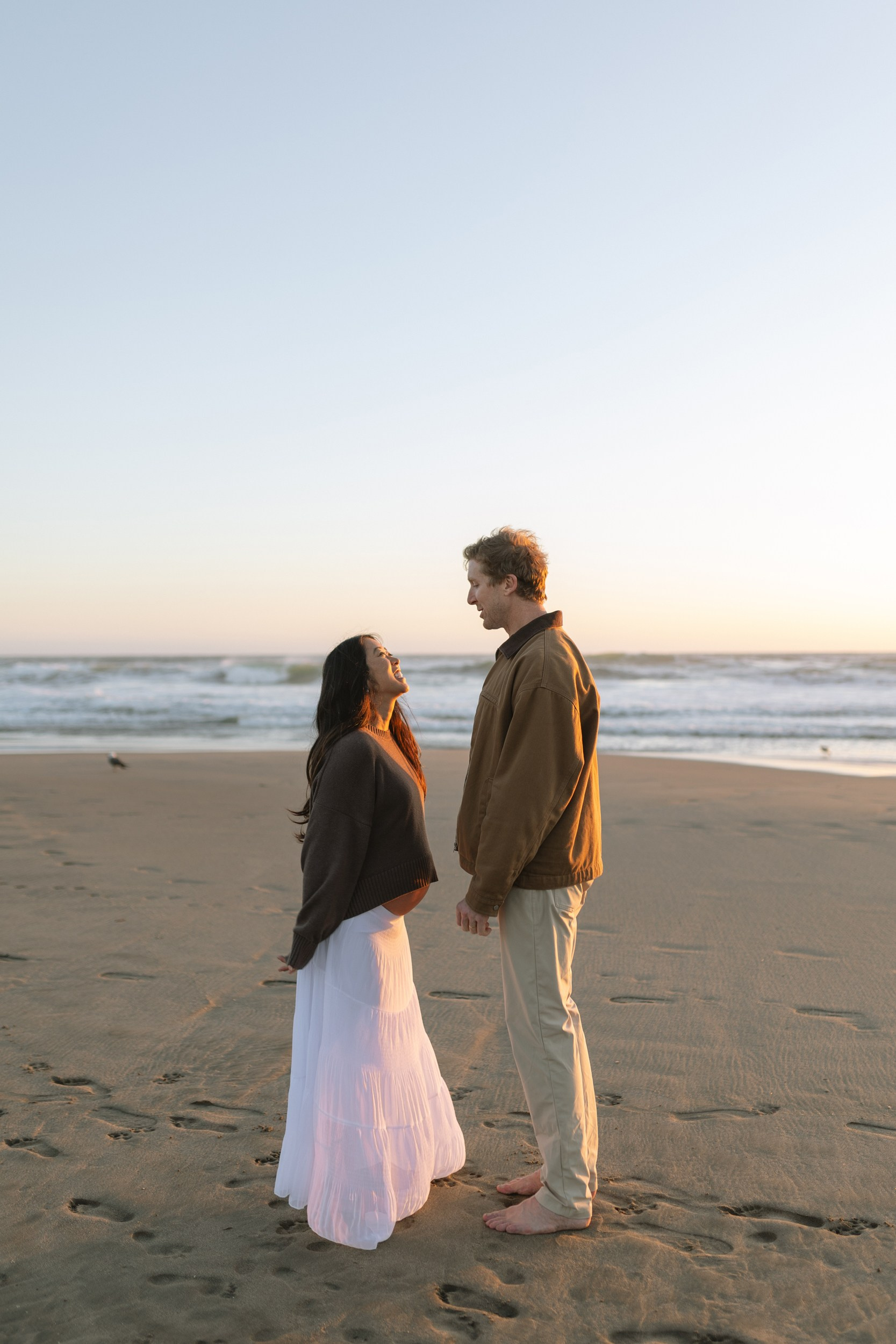 Pregnant woman and her partner embracing on Ocean Beach during golden hour