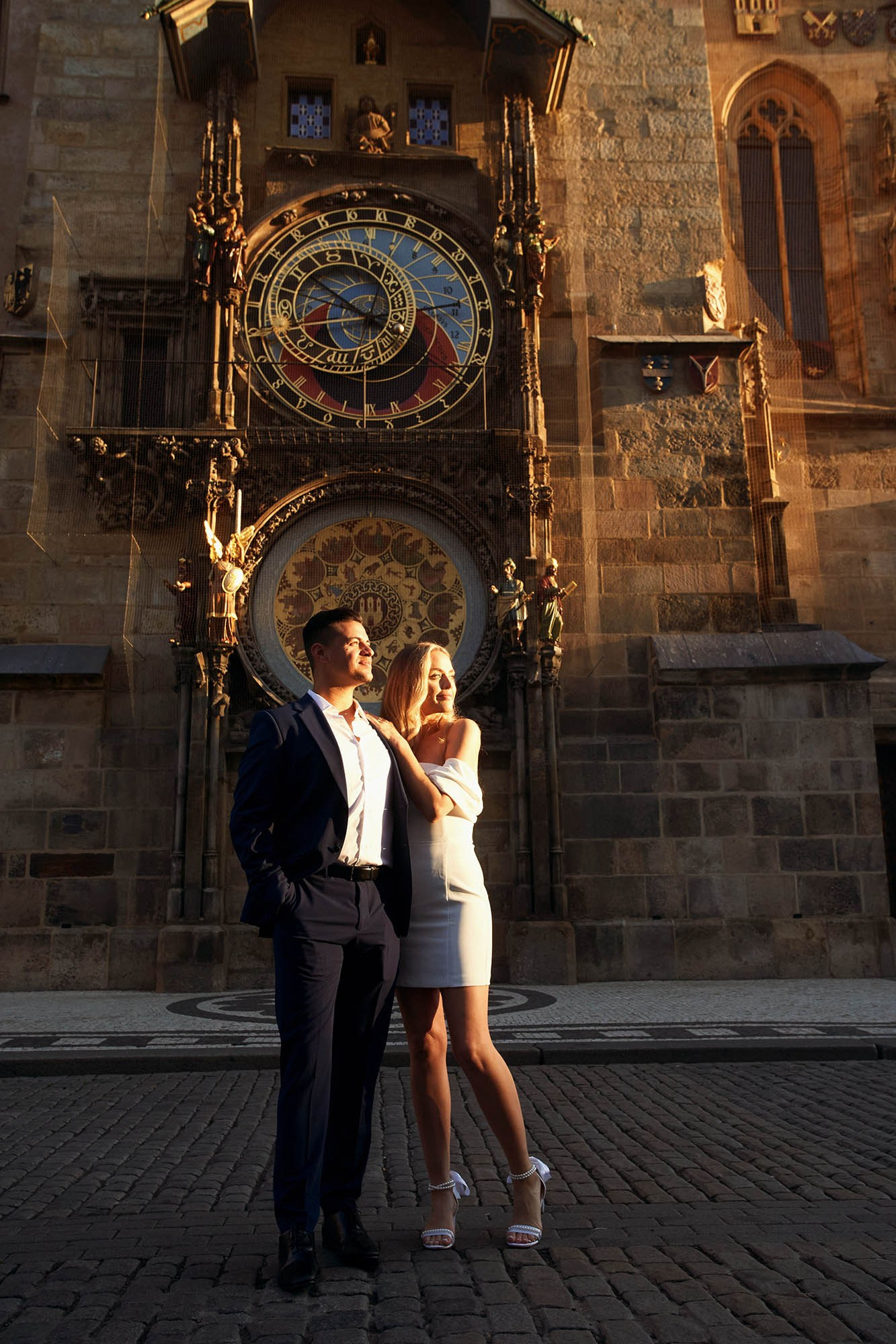 Romantic couple posing beside the Astronomical Clock during the glowing Prague dawn.
