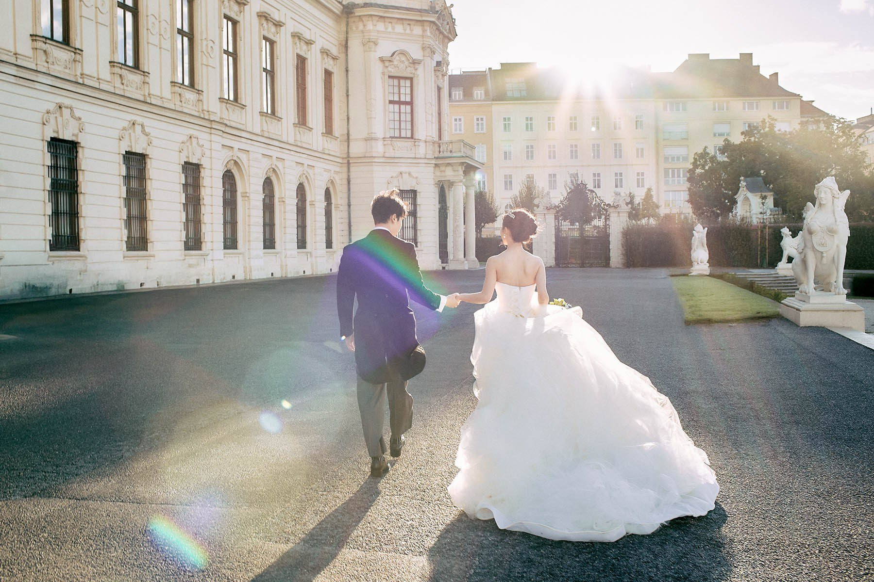 Newlyweds walking bathed in sunlight flare Belvedere Palace.