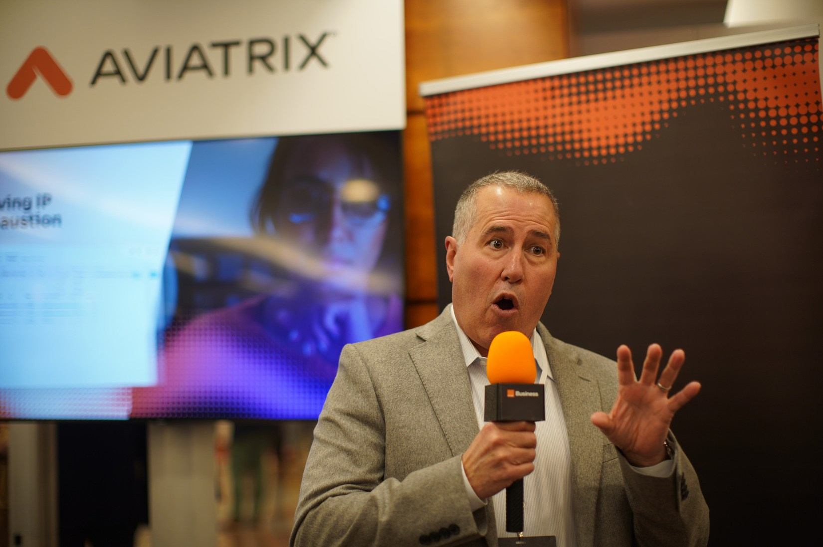 Aviatrix spokesman speaking into microphone during interview at Orange Business Sales Kick-Off exhibition, Hilton Prague.