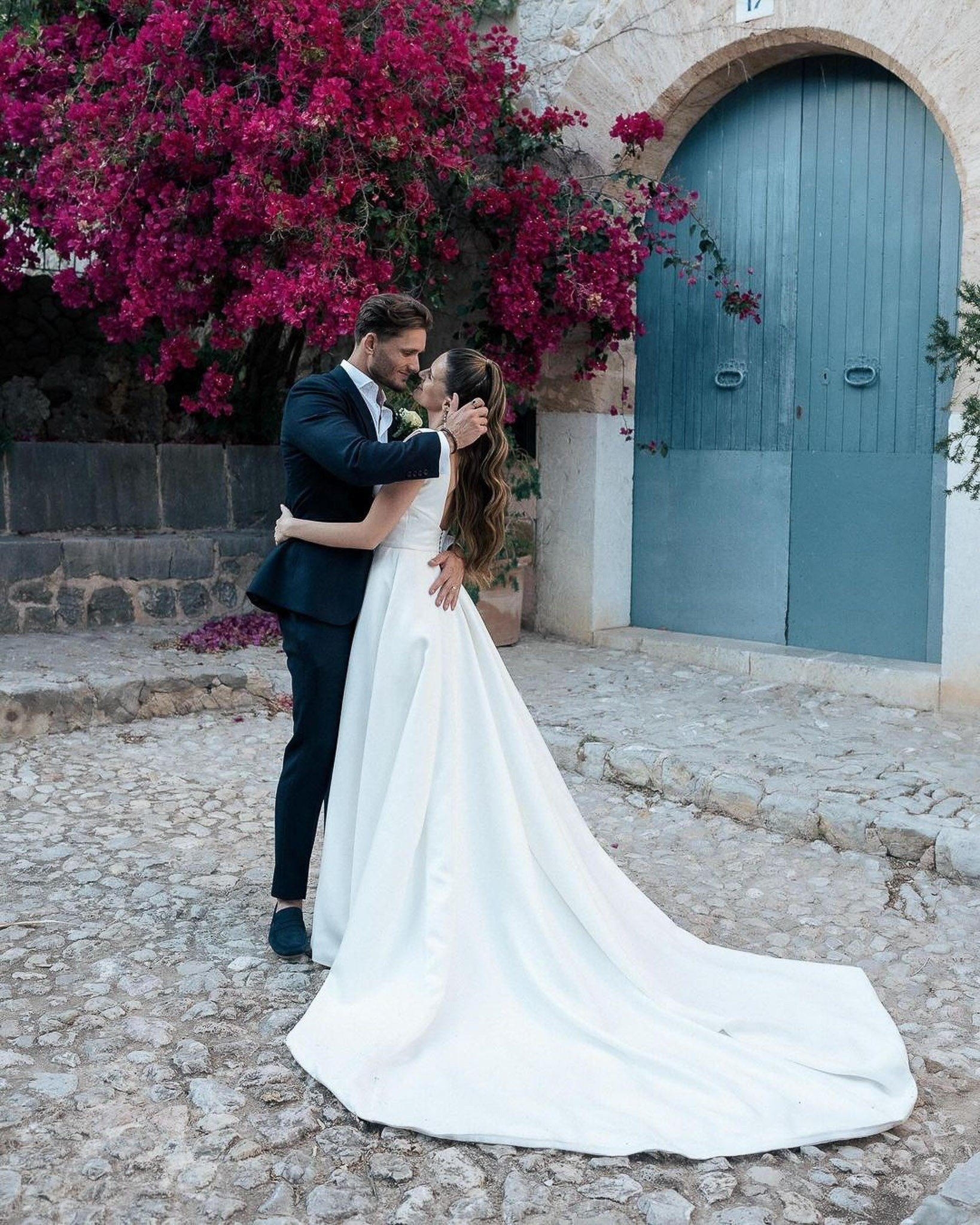 Bride and groom embracing beside a blue door and bougainvillea at their Mallorca wedding venue