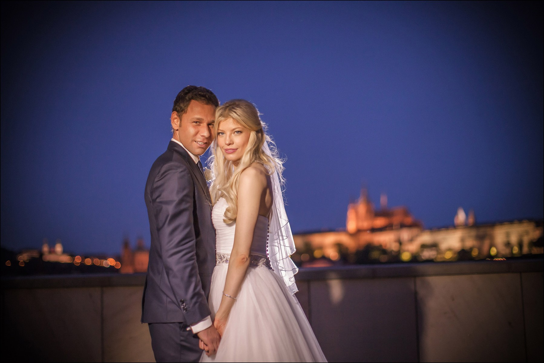 Newlyweds confident pose nighttime Prague Castle backdrop Four Seasons