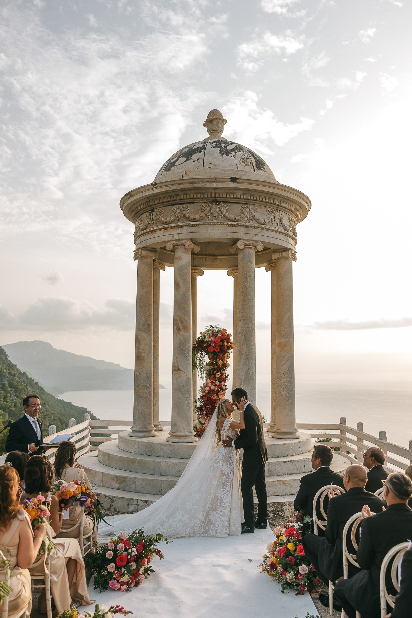 Bride and groom kissing at the Son Marroig temple as their wedding officiant looks on