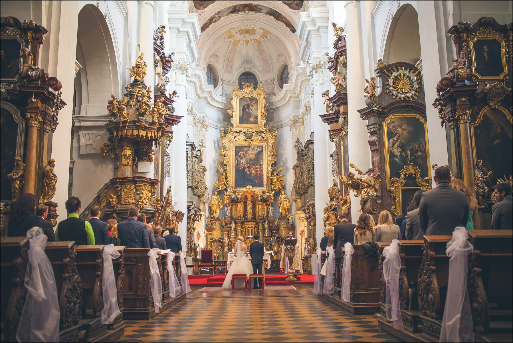 View from back of church of couple at altar St. Thomas Prague wedding