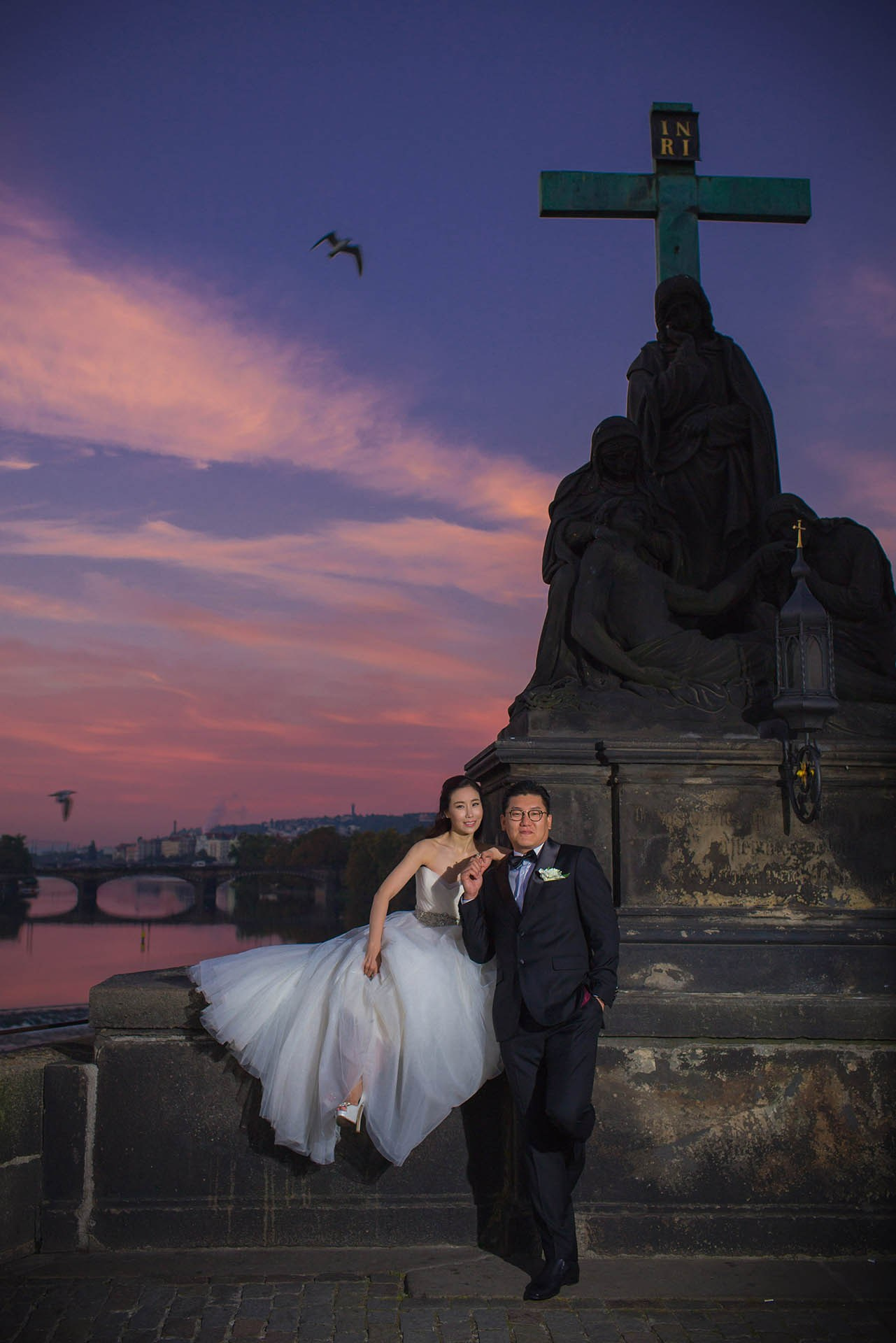 Catherine and Cedric Son pose historic statue vivid sky Prague wedding portrait.