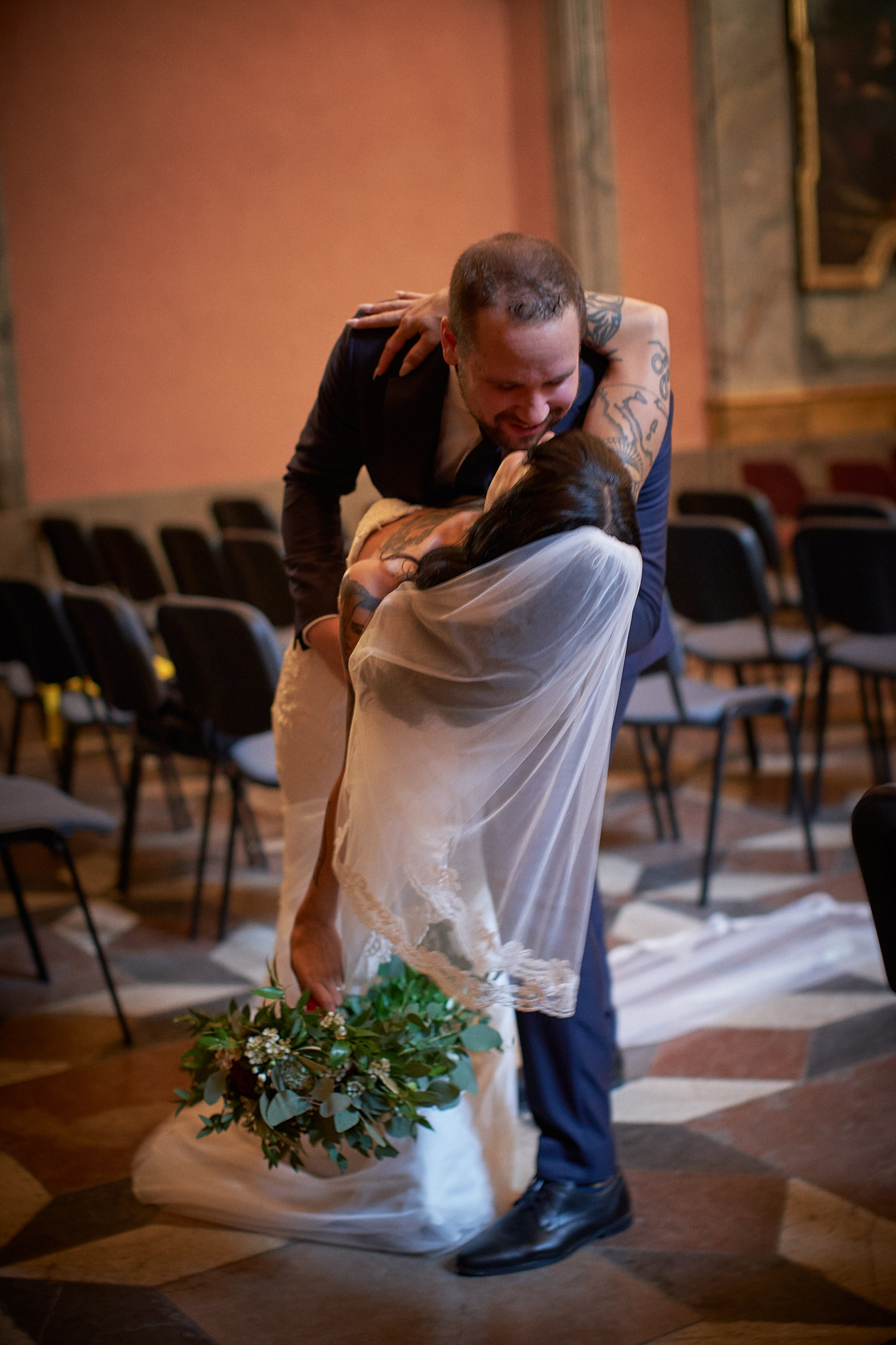Groom dipping tattooed bride in spontaneous chapel celebration.