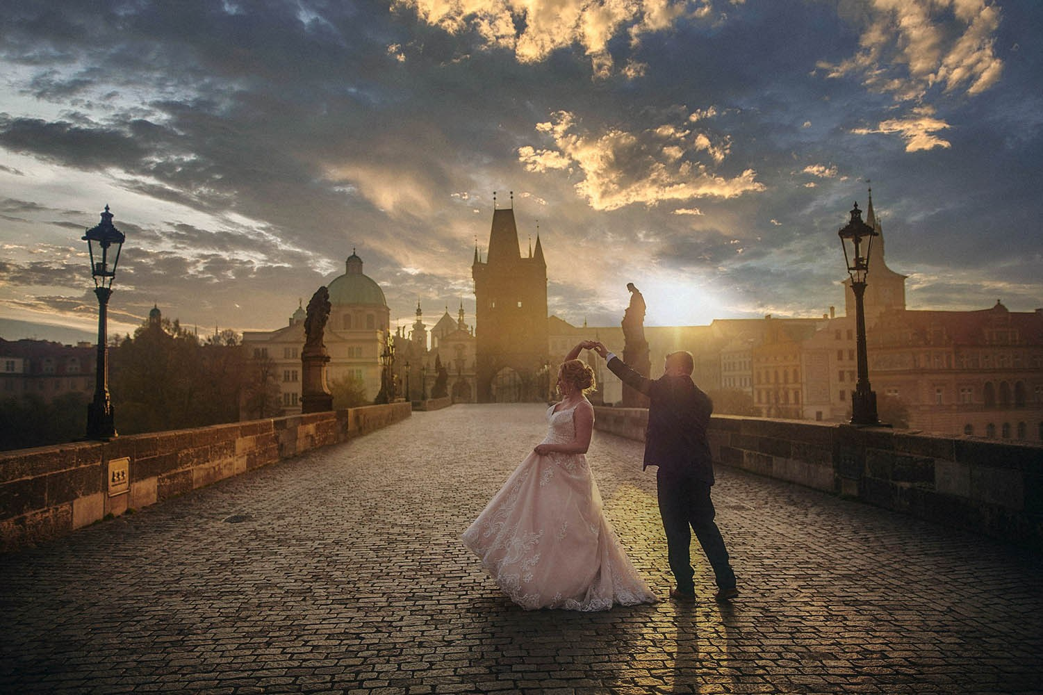 Bride and groom dance all alone atop the Charles Bridge as the sun breaks above the skyline at sunrise.