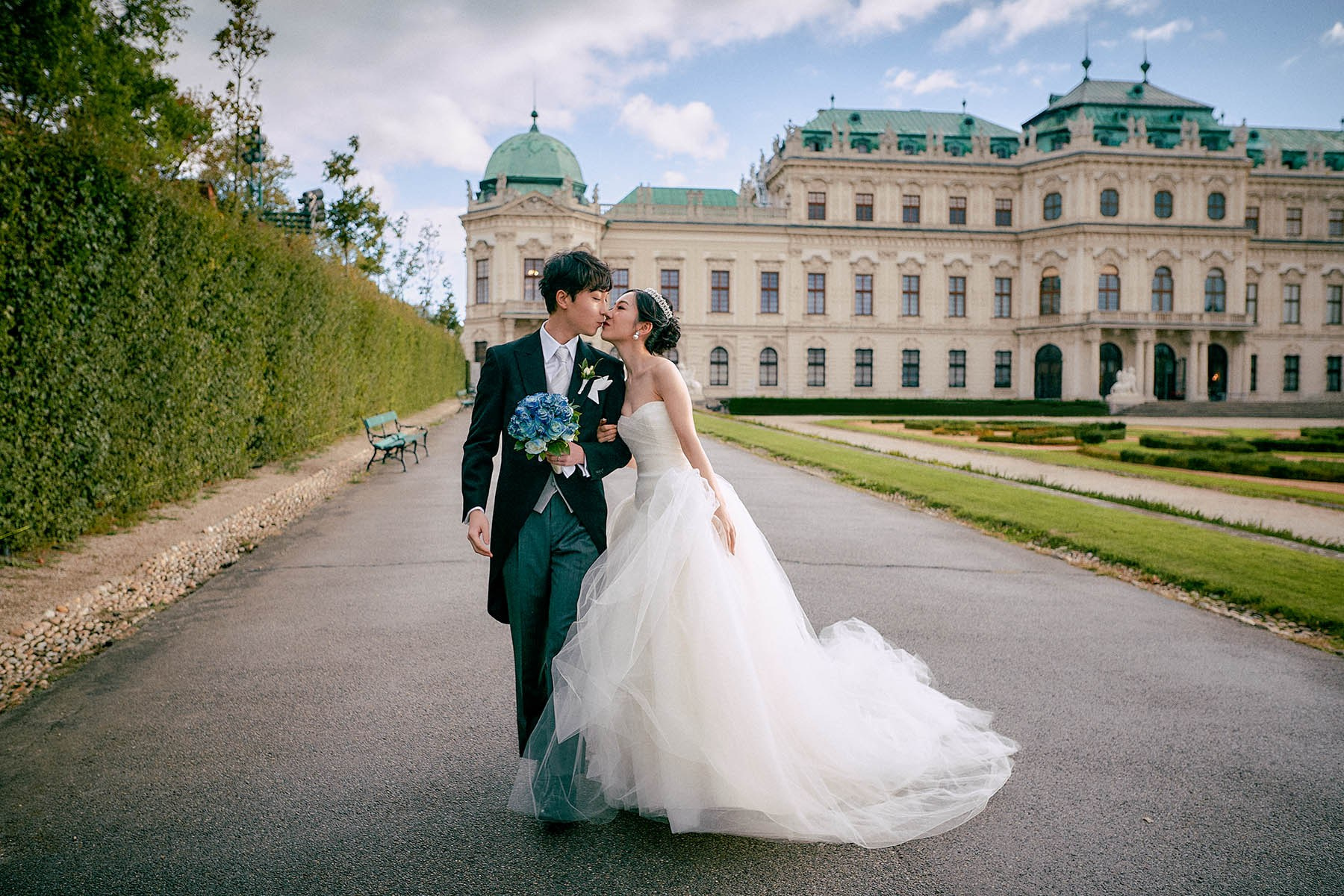 Newlyweds kissing hand in hand in Belvedere Palace gardens.