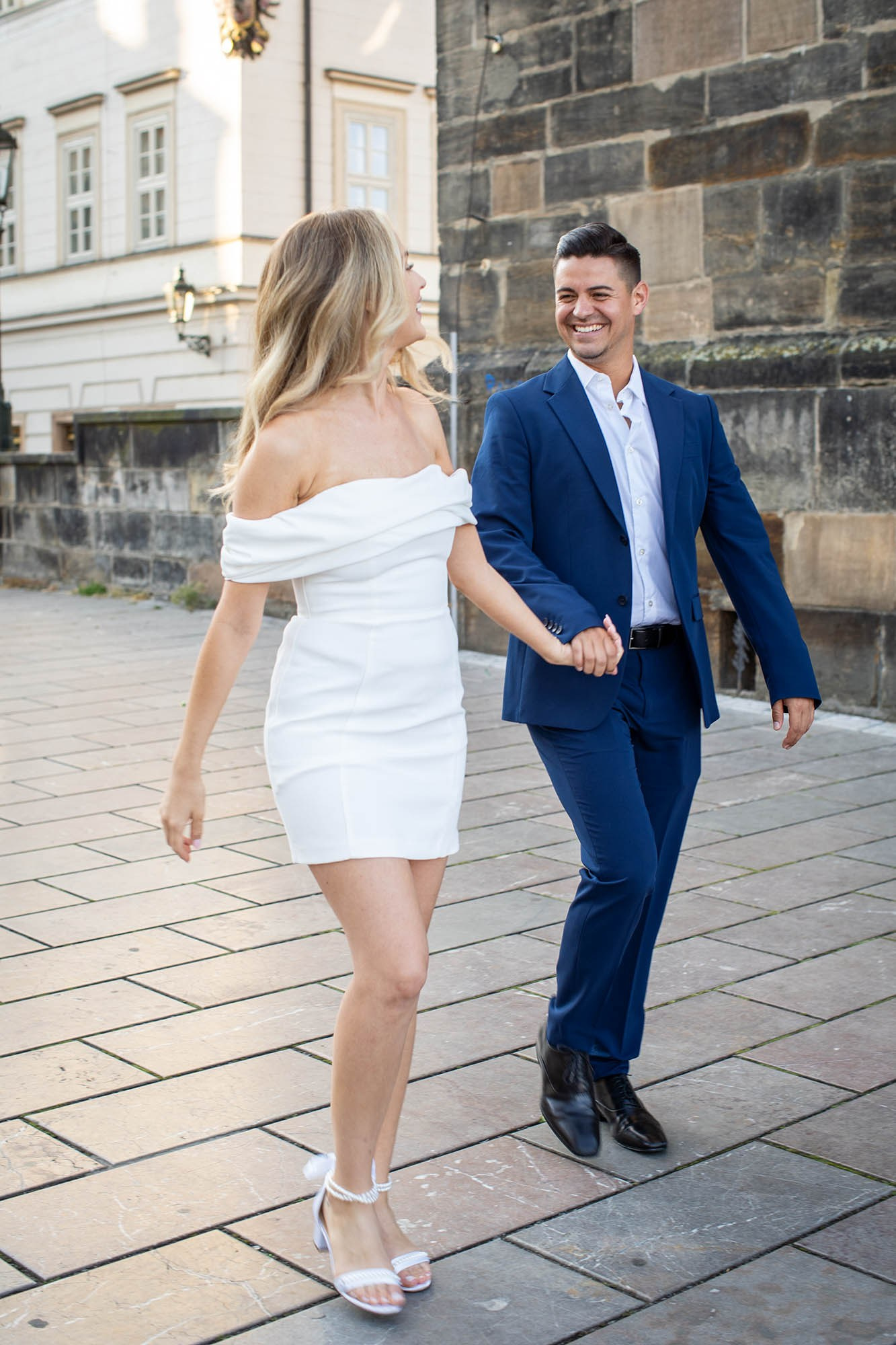 Stylish American couple walking through quiet Prague streets in soft dawn light.