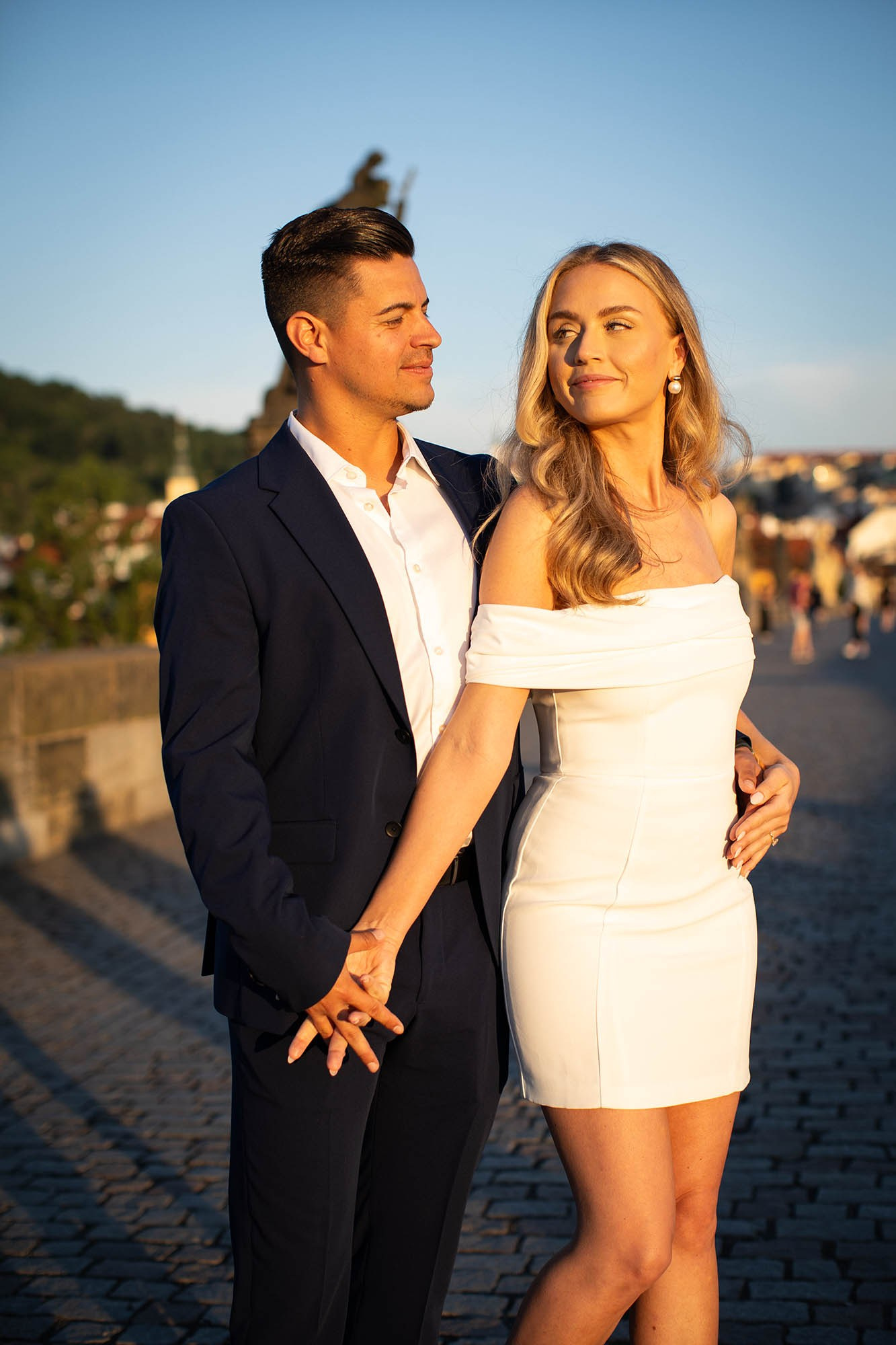 The blonde-haired woman and her stylish partner are bathed in the early morning Golden Light as statues fill their background.