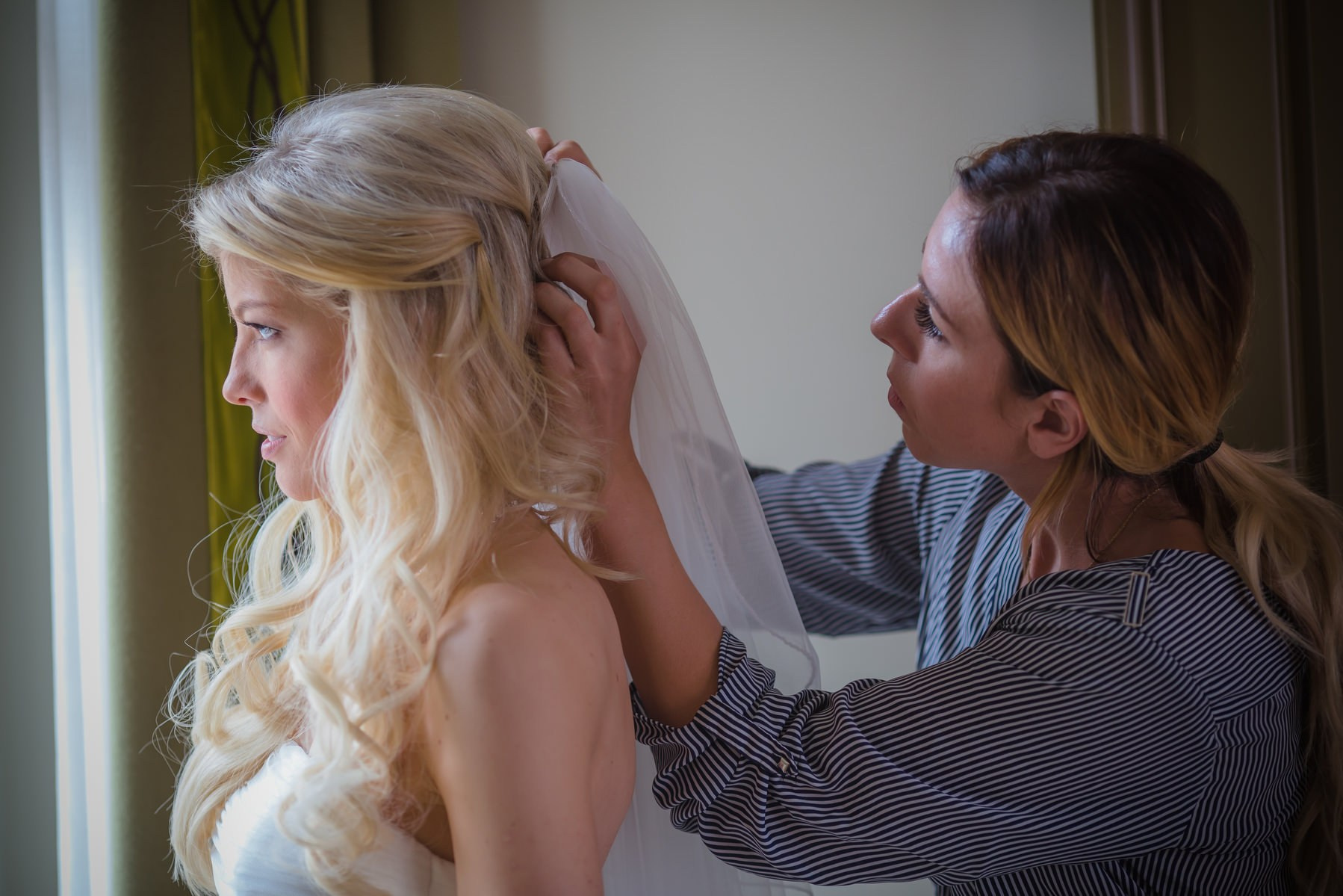 Makeup artist and hairstylist placing bridal veil on Julia at Augustine Hotel Prague