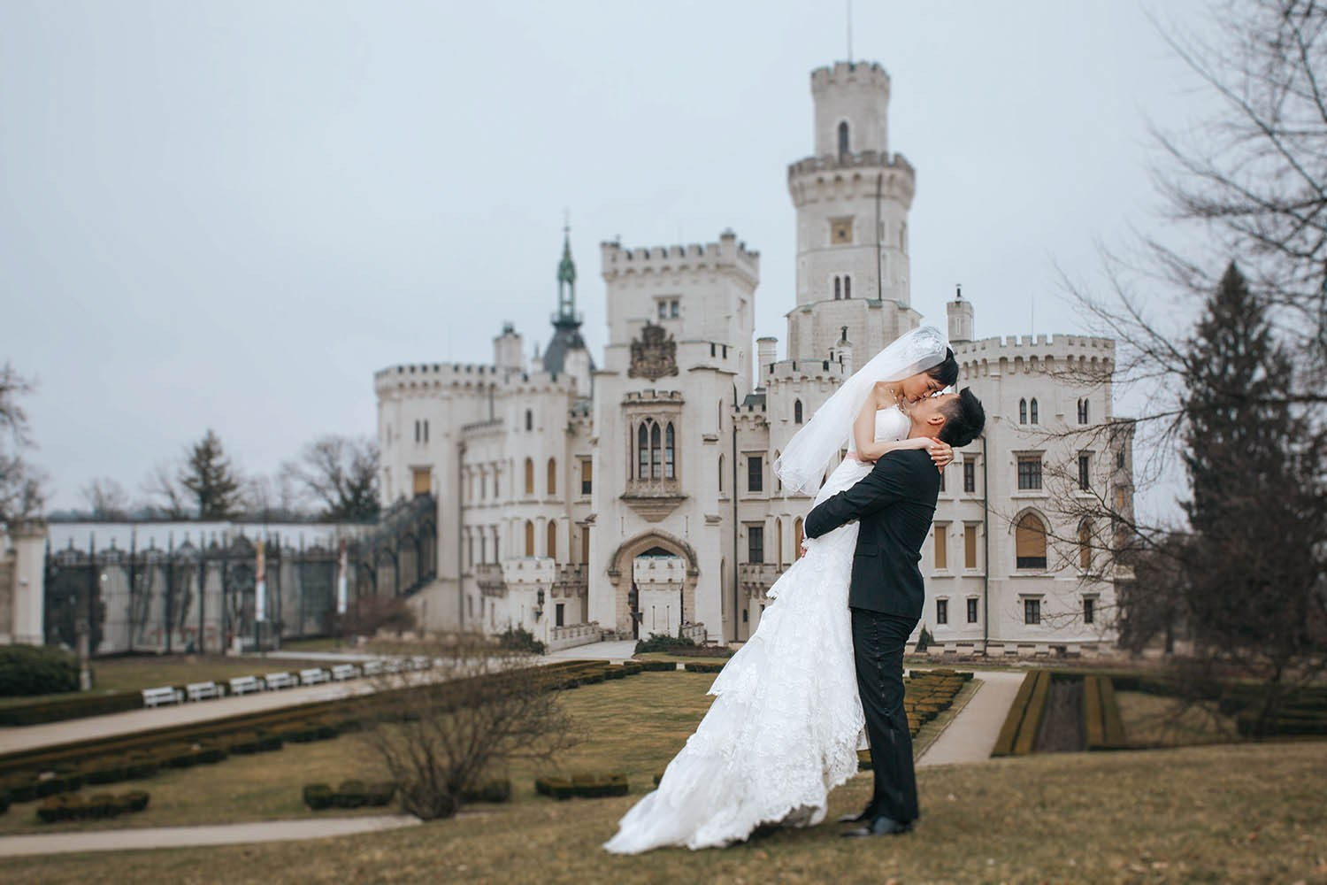 A groom holds his bride aloft as he kisses her against the backdrop of the Castle Hluboka.