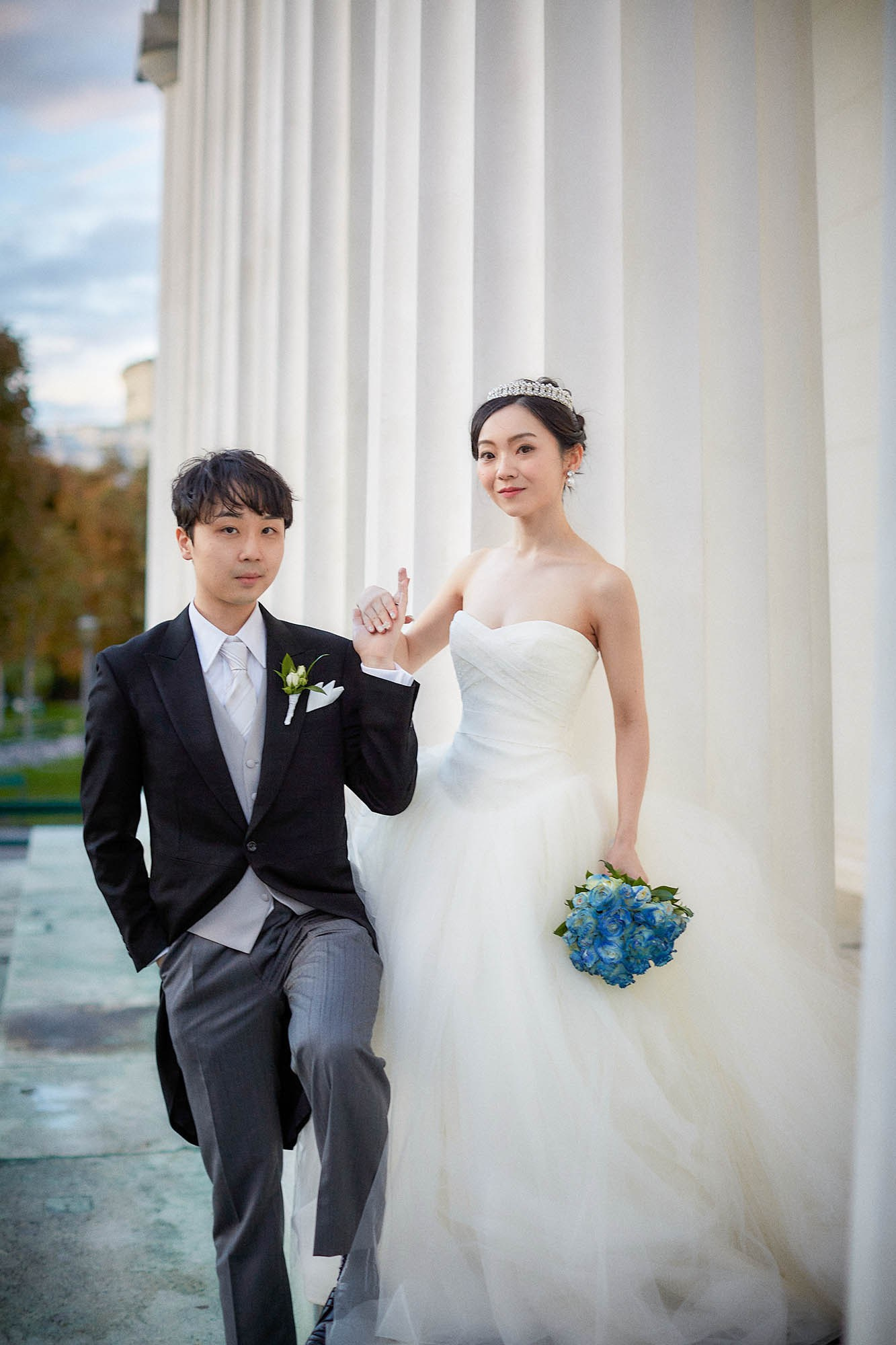 Groom holding bride's hand standing together Vienna garden.