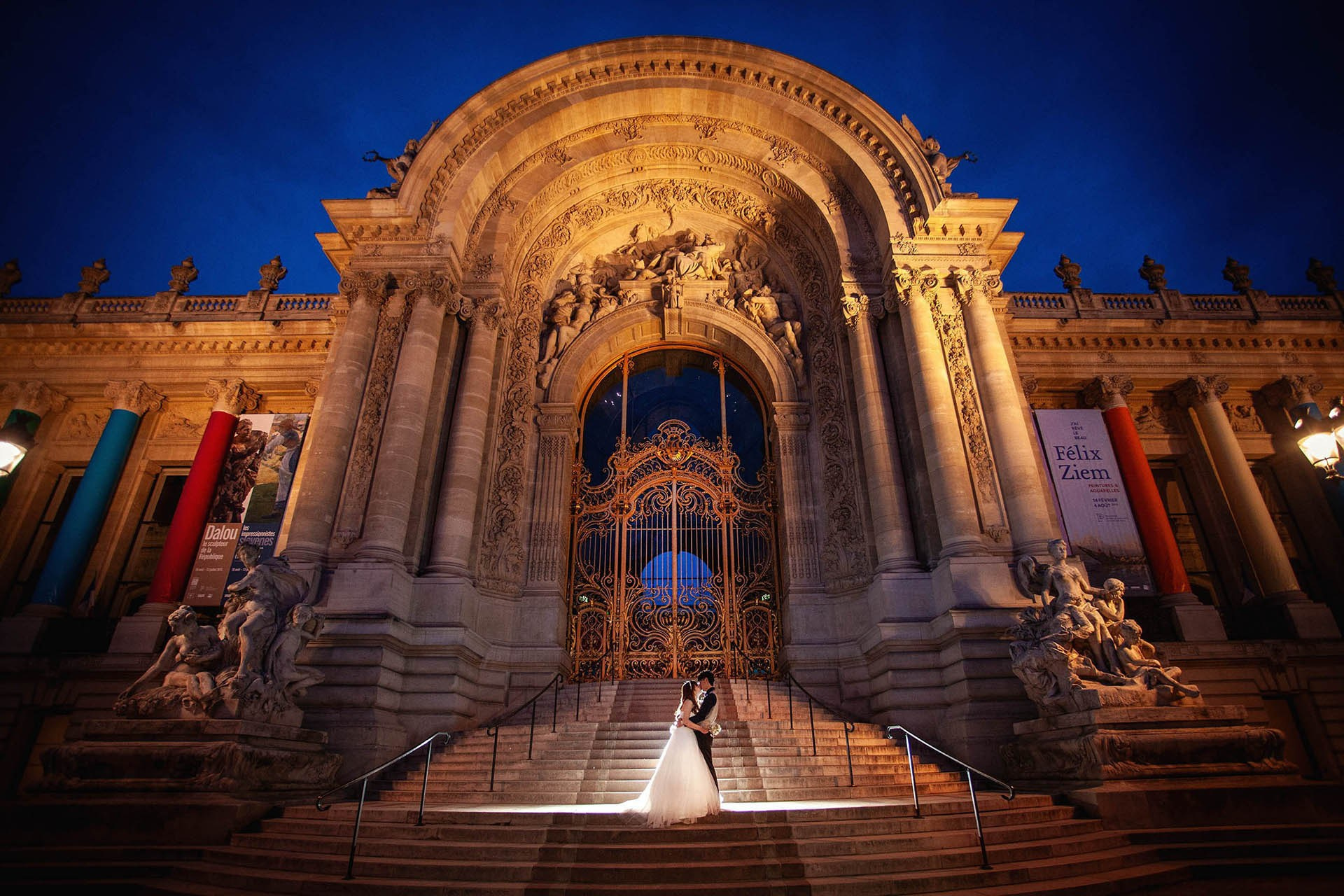 Bride and groom in front of Petit Palais golden doors at night with rim light, Paris.