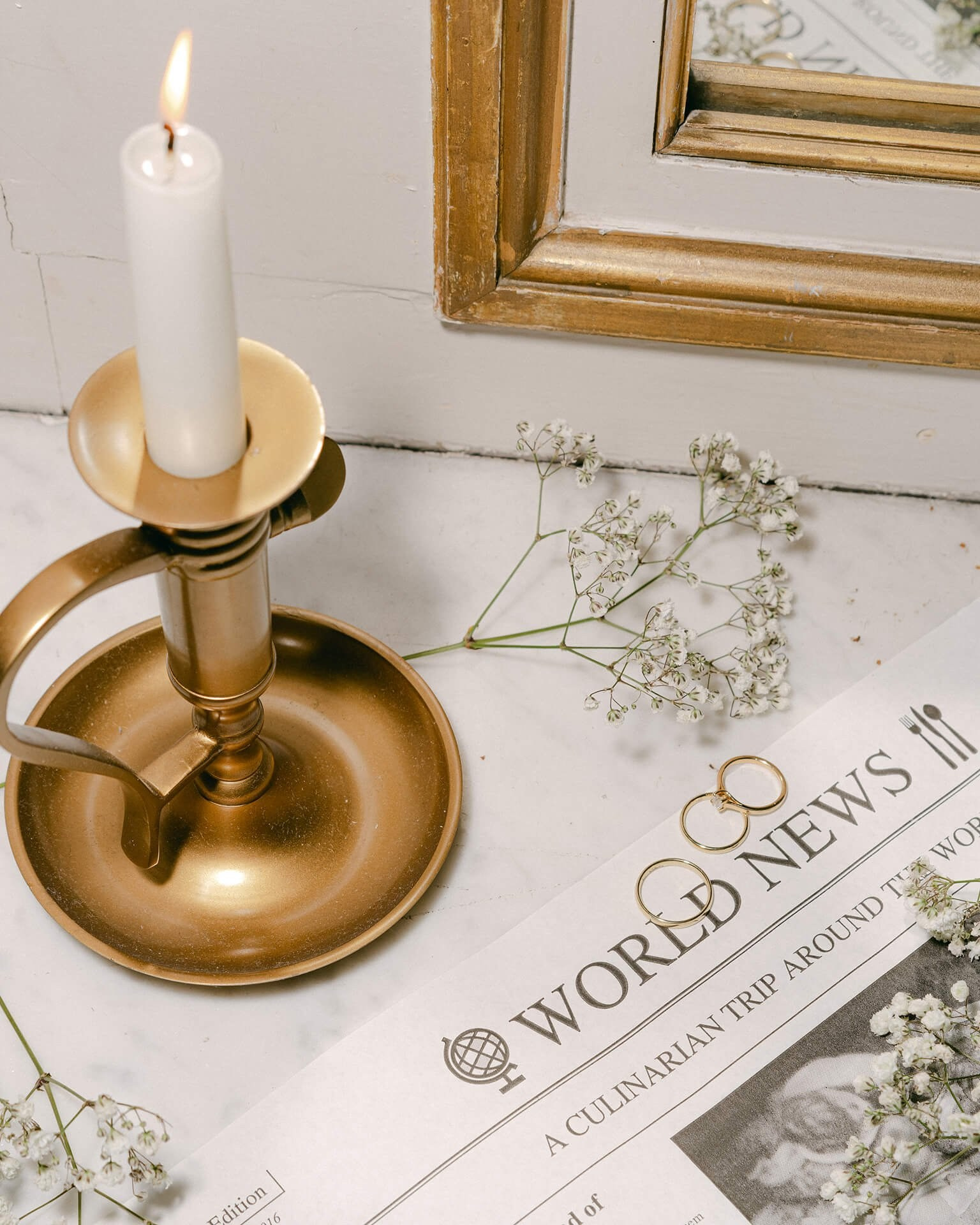 Wedding detail flat lay, brass candleholder with rings and newspaper