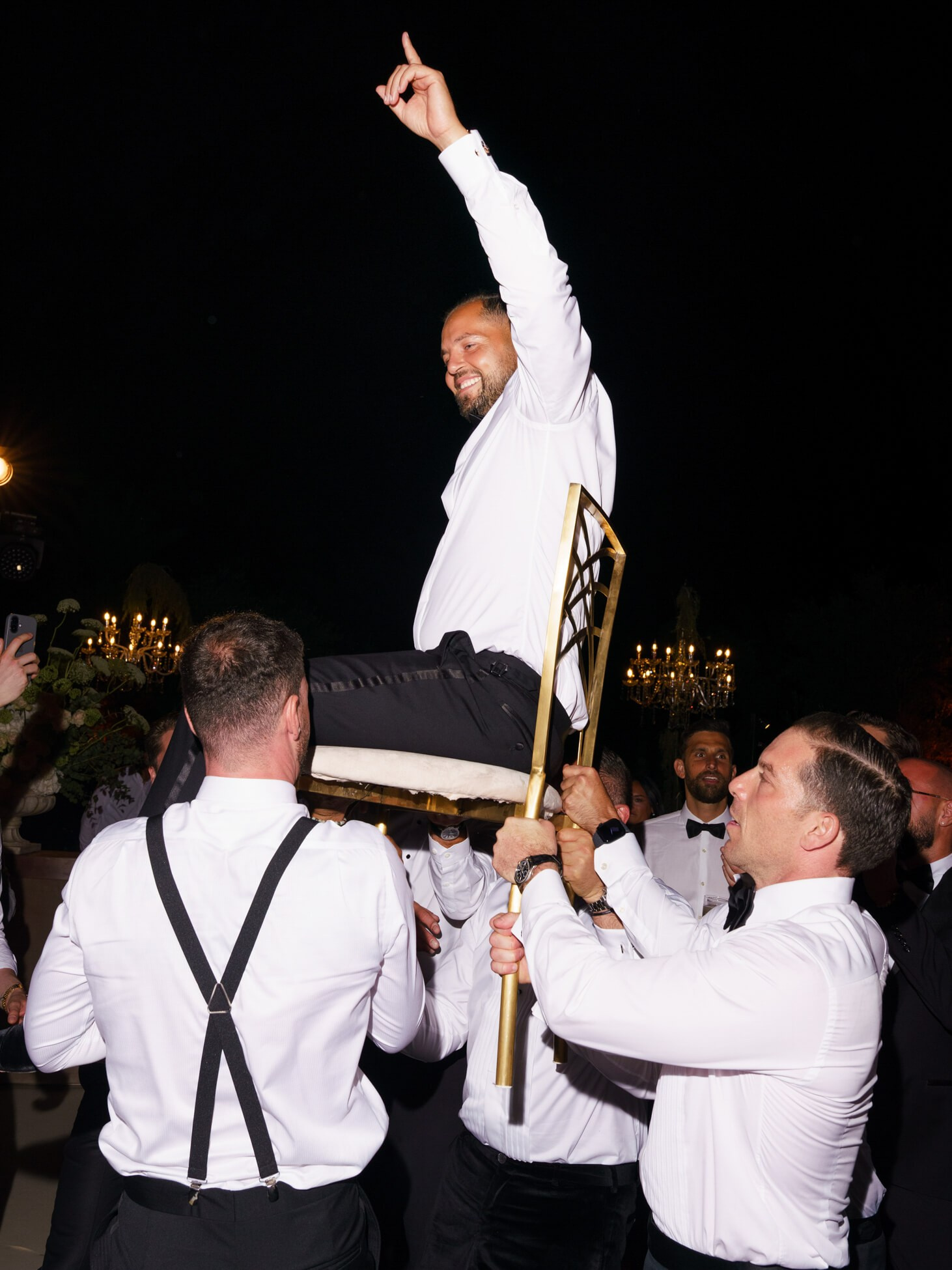 Wedding reception dance, guests lift groom on chair