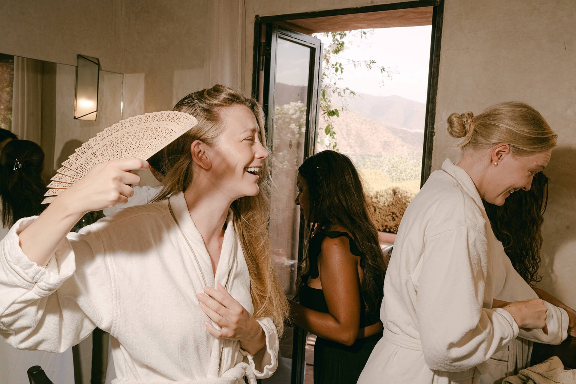 Wedding morning prep, woman in robe fans herself by window