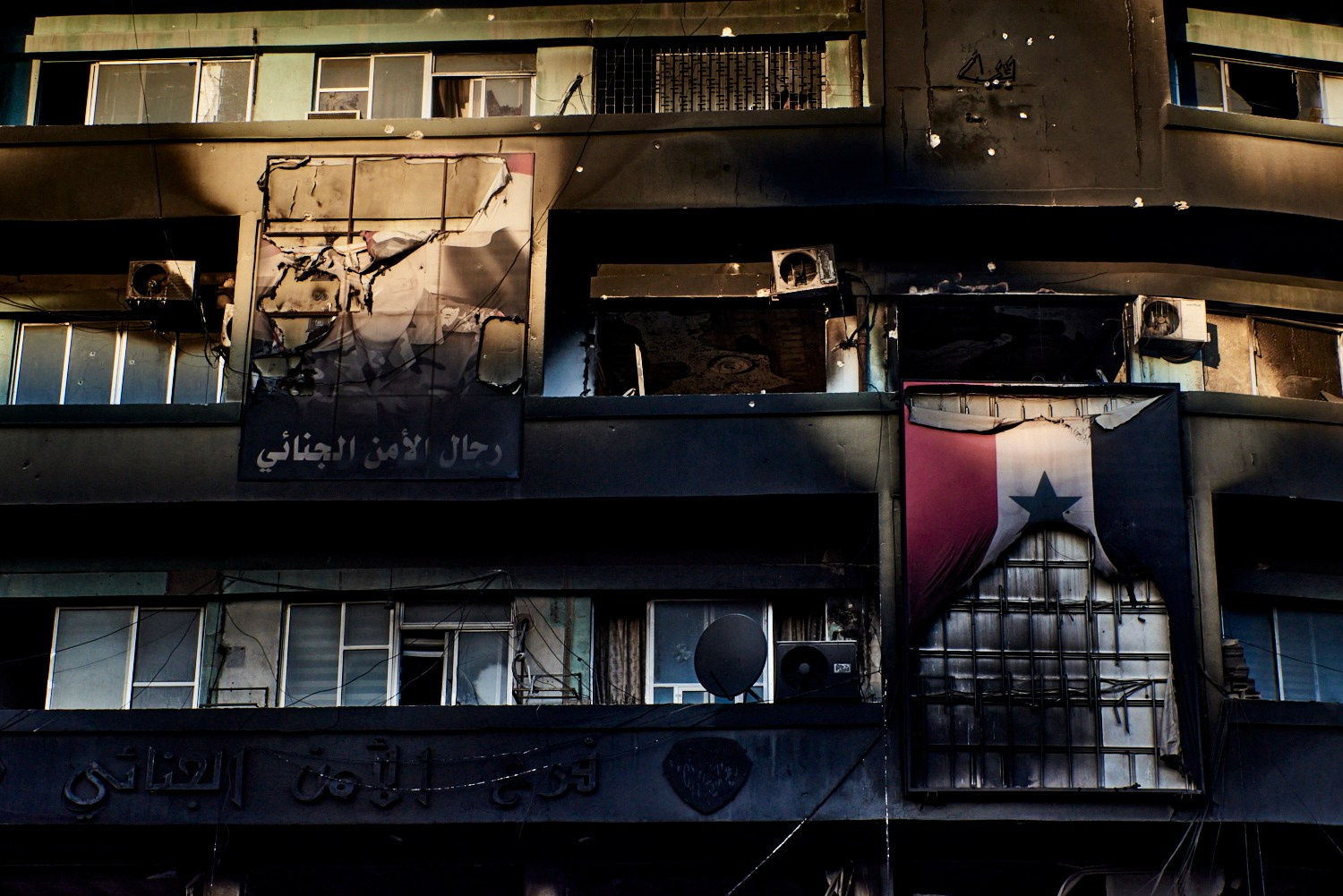 Damas, 18 décembre 2024 – Portrait de Bachar al-Assad et drapeau du régime déchu brûlés, sur la façade d'un bâtiment administratif saccagé.