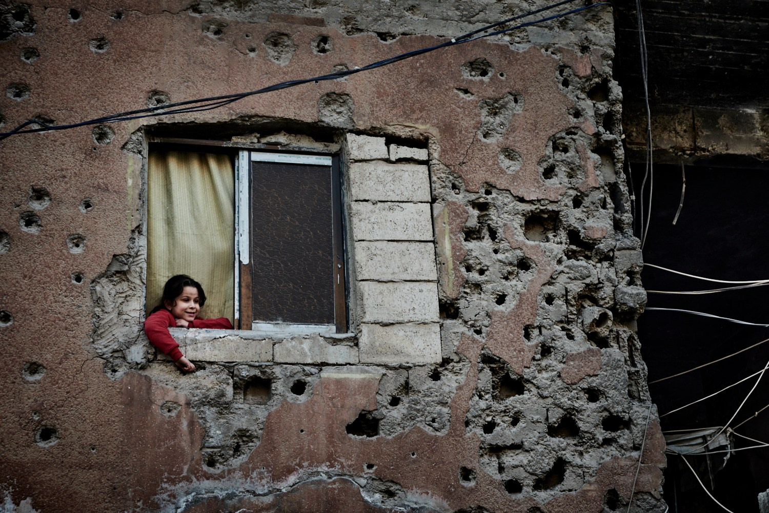 Raqqa, 9 février 2025 – Une fillette à la fenêtre de sa maison, aux murs criblés d'impacts de balles et de projectiles, dans le centre de Raqqa. L'ancienne capitale de l’État islamique a été le théâtre d'une grande bataille en 2017, à l'issue de laquelle les Forces Démocratiques Syriennes, épaulées par l'aviation de la coalition internationale, en ont chassé les djihadistes.