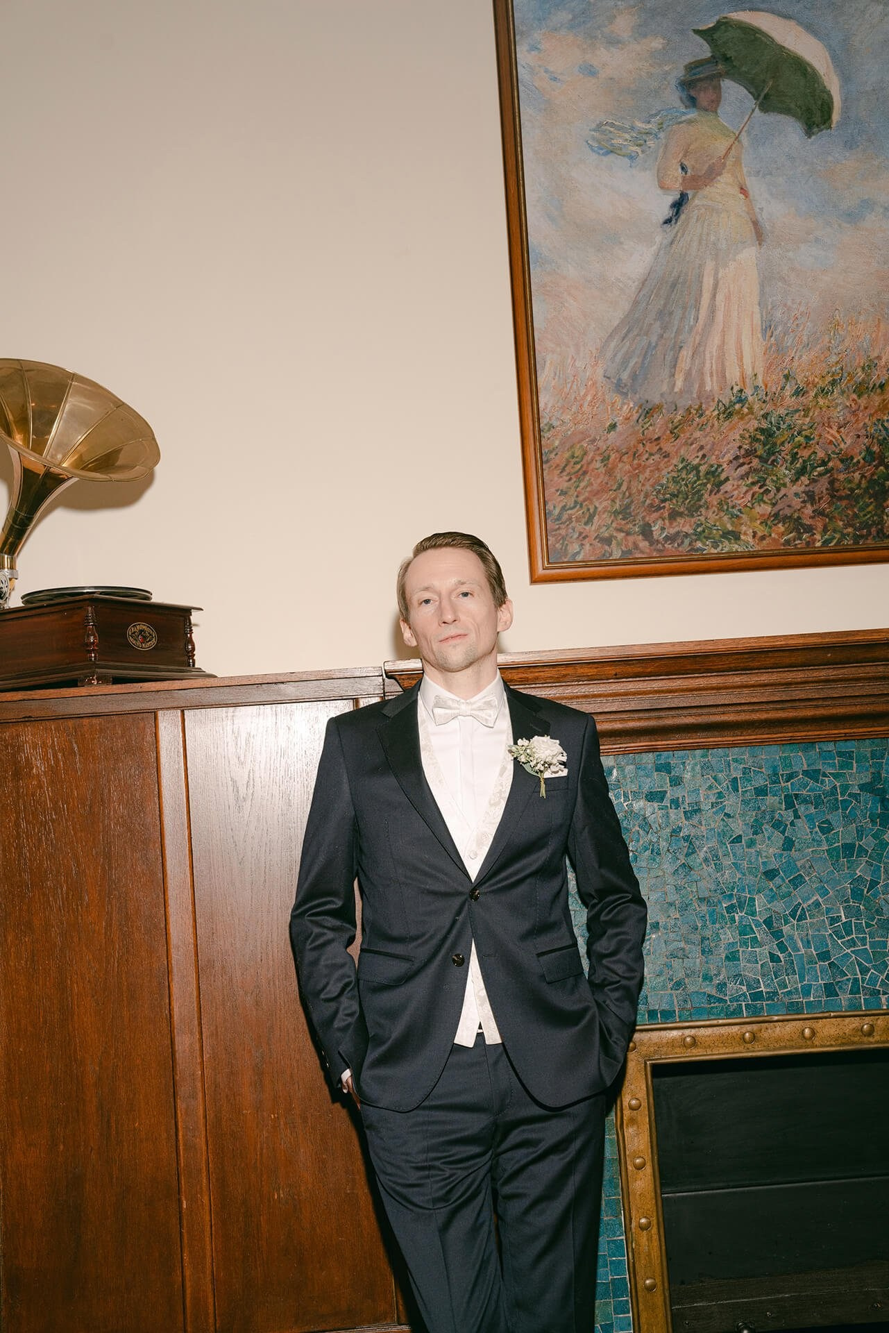 Groom portrait indoors beneath painting, editorial wedding moment