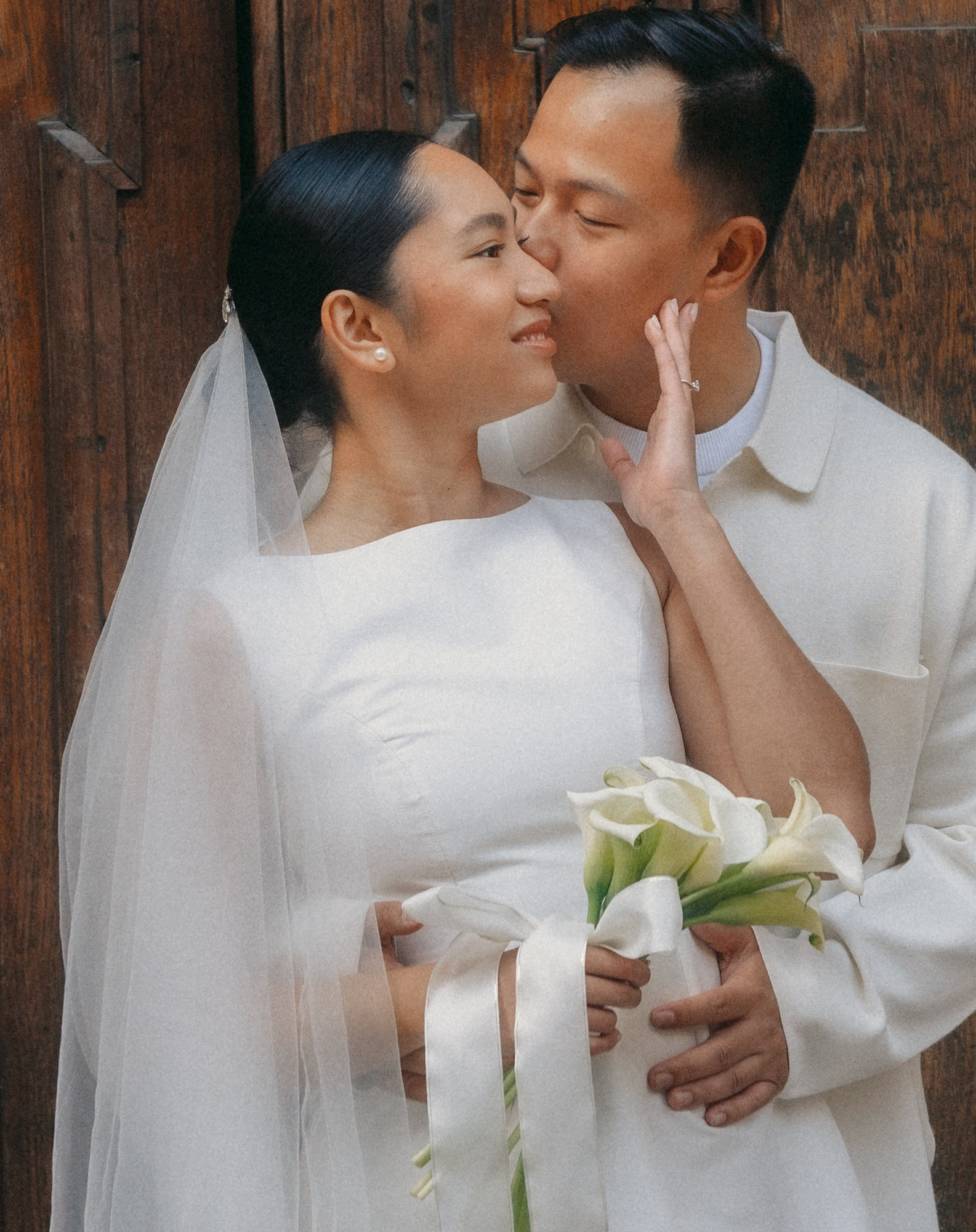 Romantic wedding photo of a bride and groom sharing a tender kiss in an elegant urban setting. The bride holds a refined white calla lily bouquet, symbol of purity and timeless beauty. Emotional and natural wedding photography. wedding photographer, bride and groom kiss, calla lily bouquet, romantic wedding, wedding photography, couple portrait, elegant wedding, urban wedding, love story, destination wedding