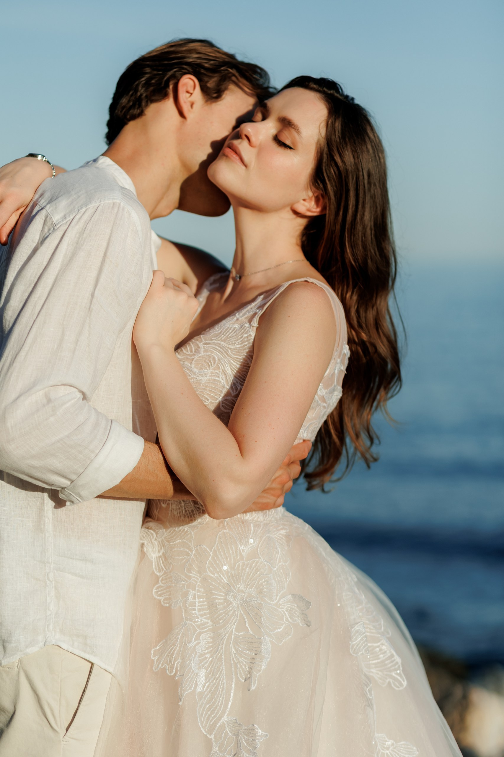 Brautpaar steht nebeneinander am Felsstrand, Totale mit Meer und Abendhimmel, Hochzeitsfotografin Costa Blanca