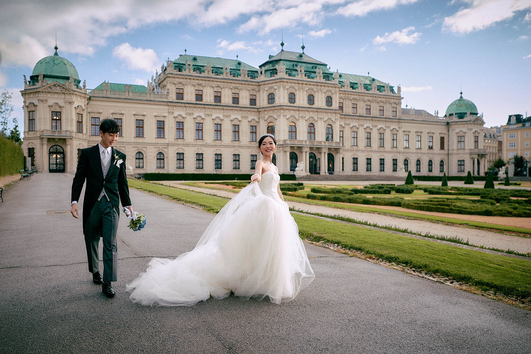 Radiant bride smiling as sun emerges in Belvedere gardens Vienna.