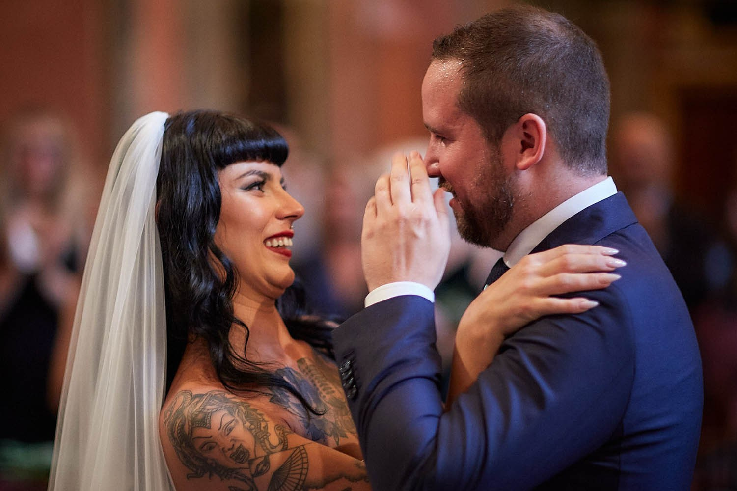 Bride beaming at teary-eyed groom during intimate ceremony moment.