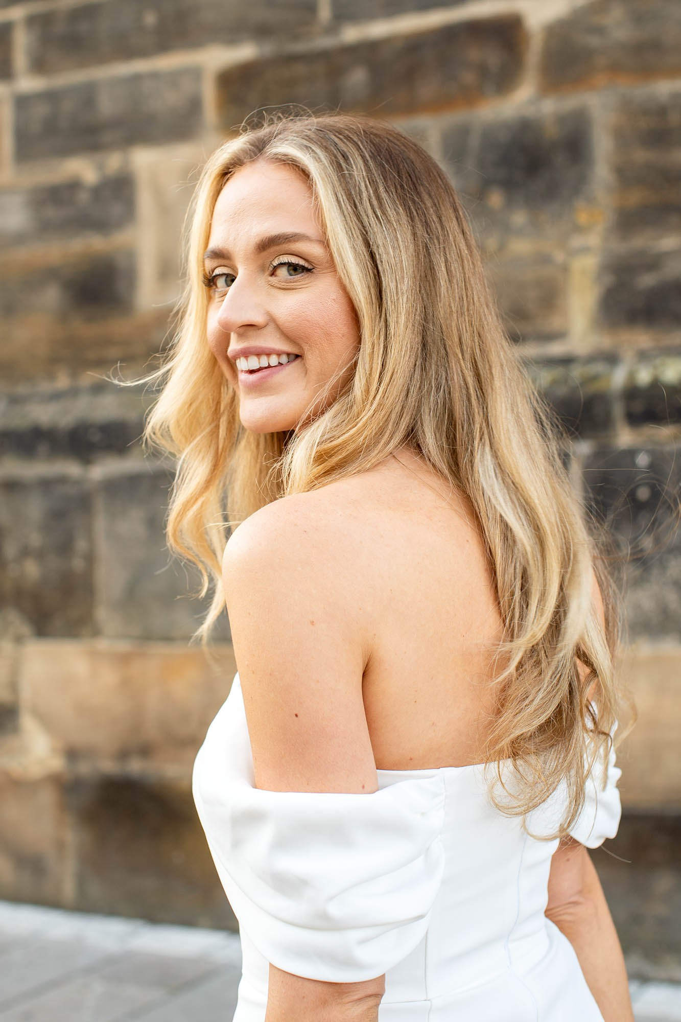 Smiling blonde woman in a white dress looking over her shoulder toward the camera.