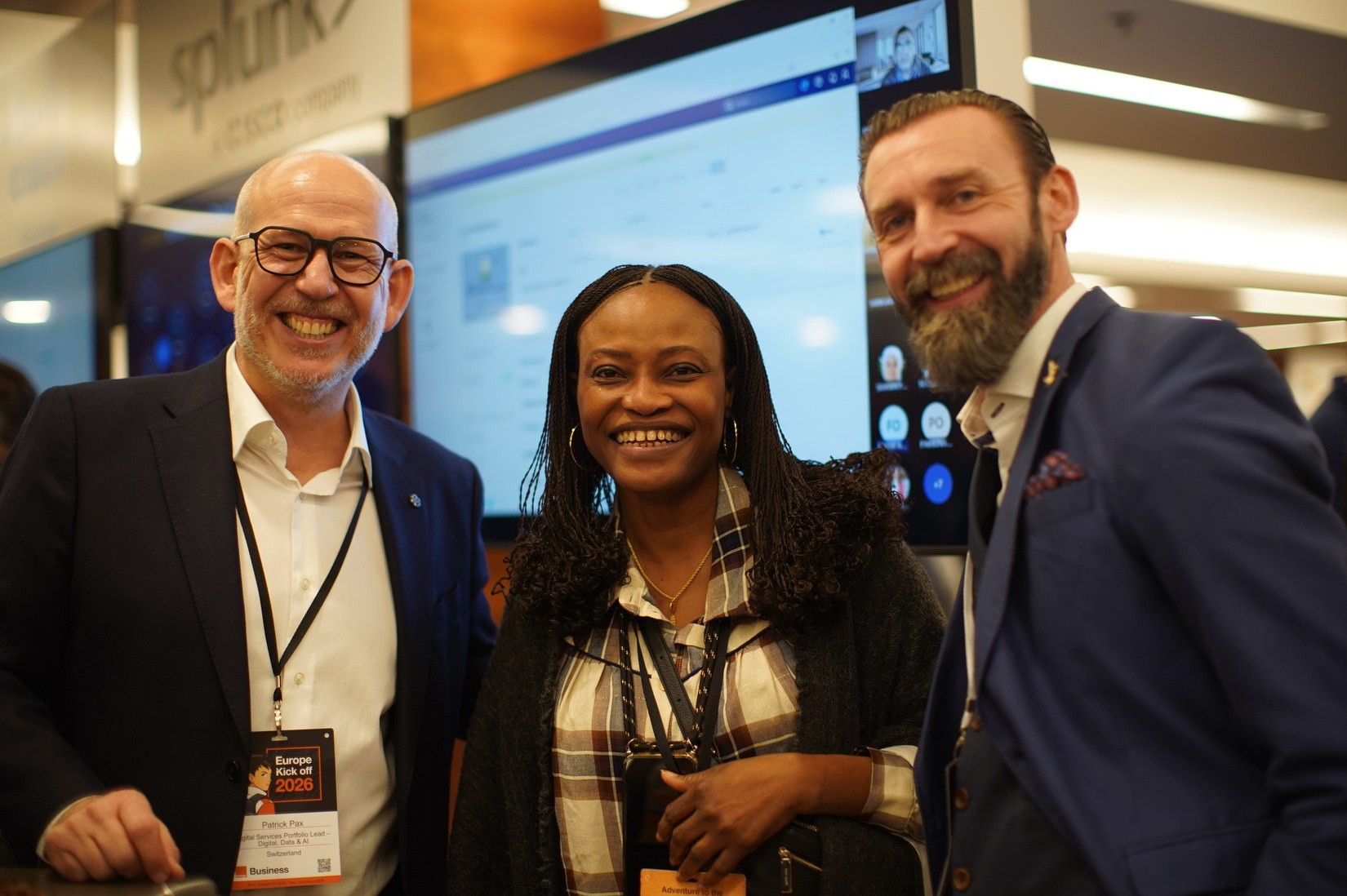 Two men and one woman smiling for group photo in exhibition area, Orange Business conference Hilton Prague 2026.