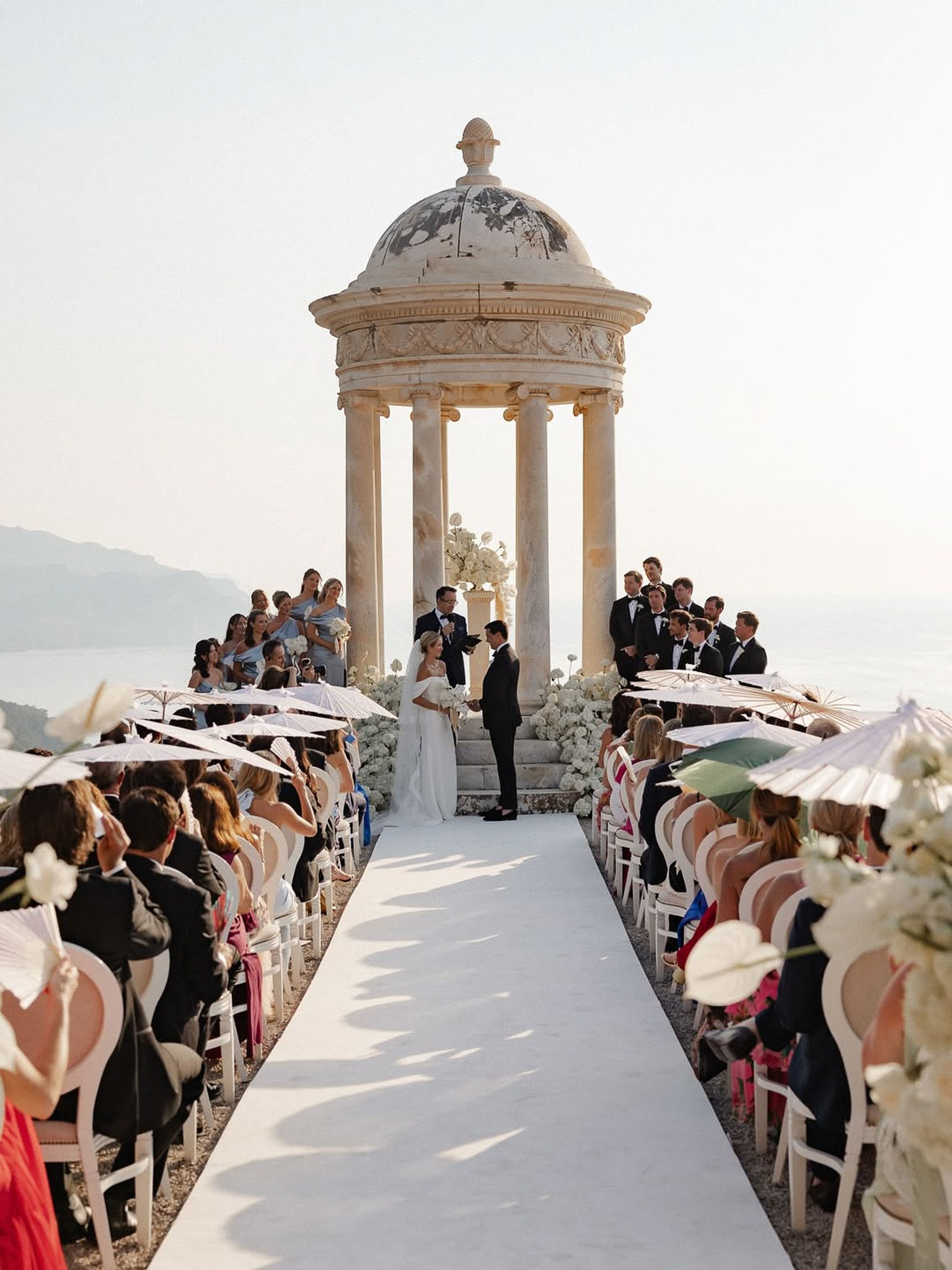 Wide shot of the bride and groom exchanging vows at Son Marroig with guests seated on either side of the aisle