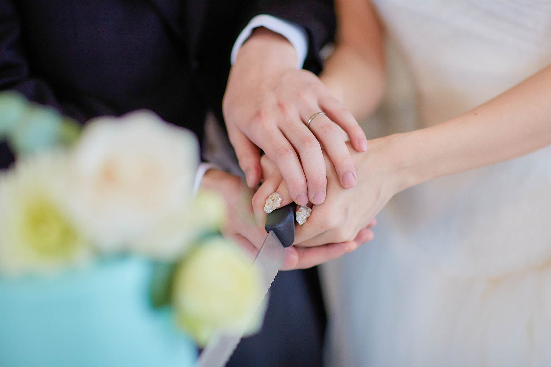 Close-up of bride's nails during cake cutting with groom.