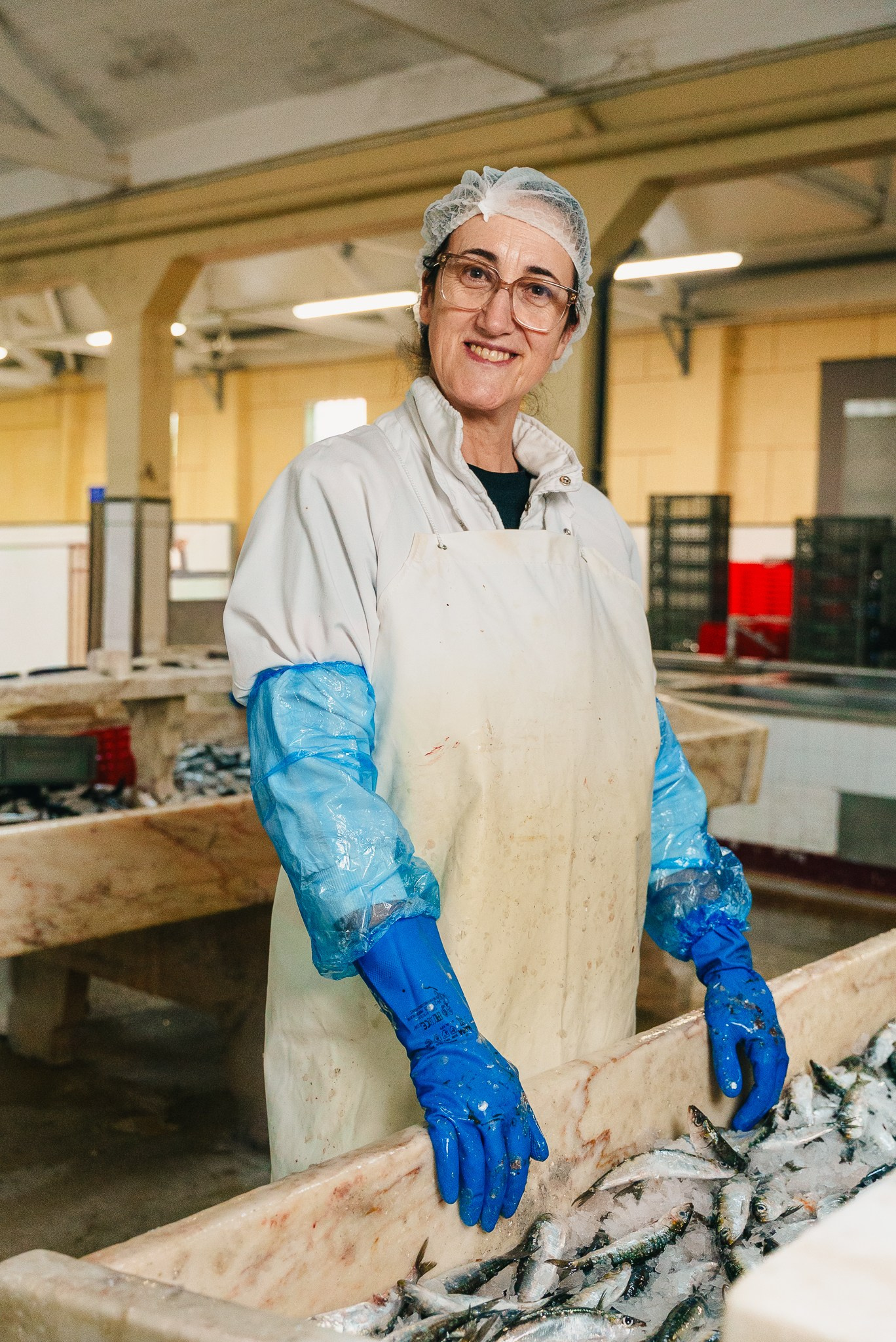 Fotografia industrial e de retrato com uma trabalhadora de bata e luvas numa linha de produção de conservas de peixe, captada no norte de Portugal pela Khave Media