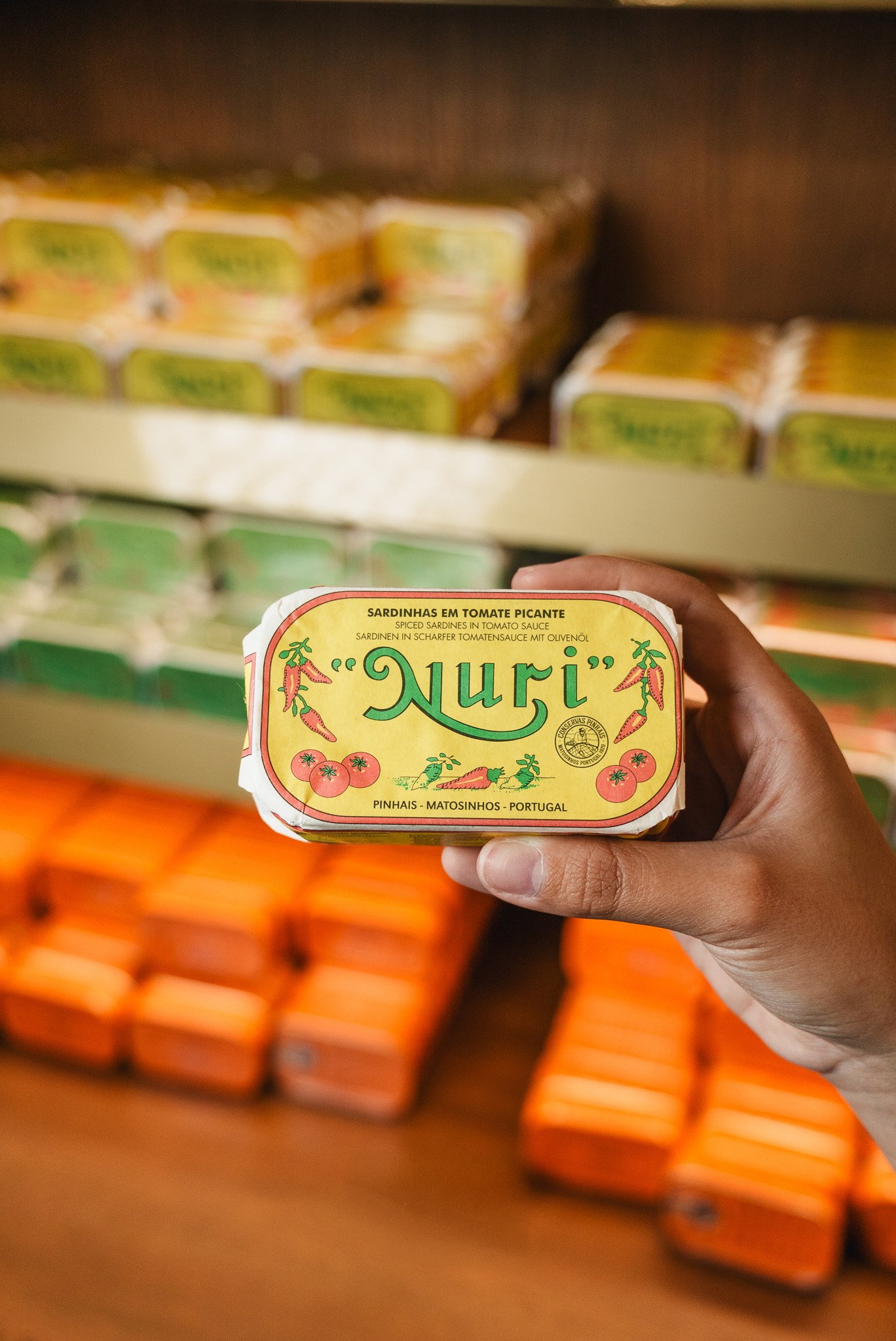 Fotografia de produto com pormenor de uma mão a segurar uma lata de conservas artesanais em frente a um expositor de madeira, produzida pela Khave Media