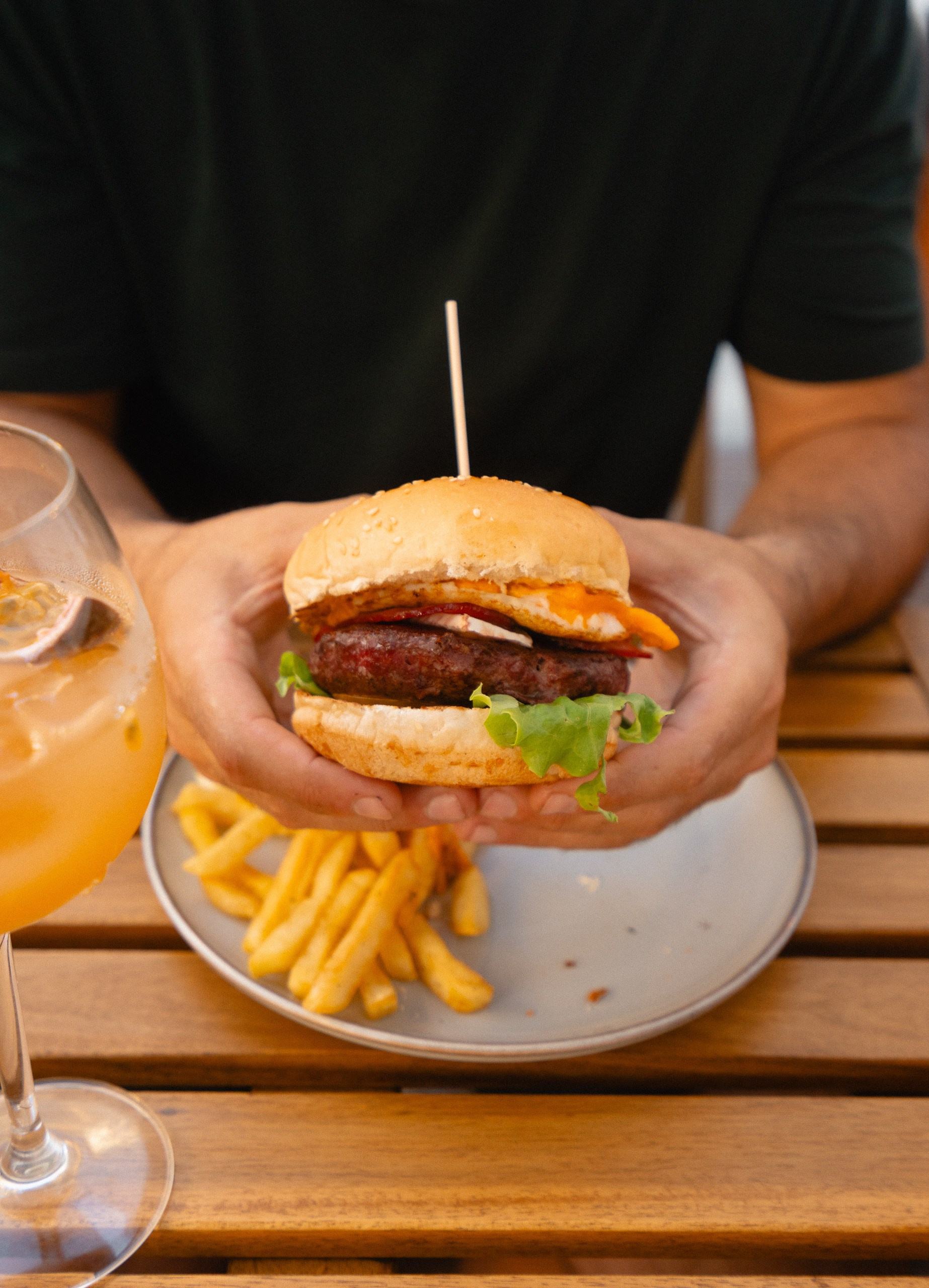 Fotografia lifestyle e gastronómica de uma pessoa a segurar um hambúrguer artesanal sobre o prato com batatas fritas, captada pela Khave Media
